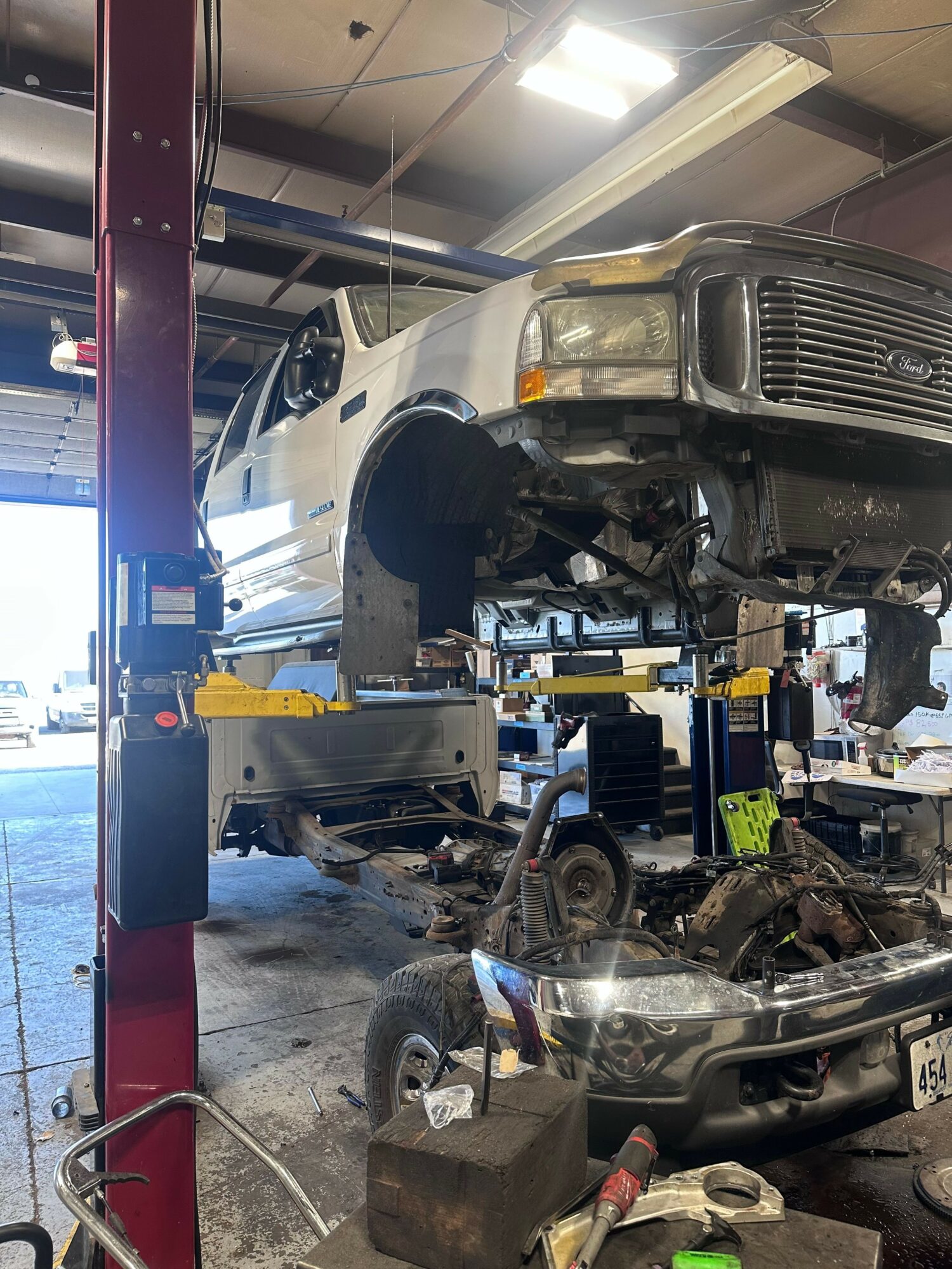 Vehicle lifted on a hydraulic lift inside a garage, with parts removed and tools nearby.