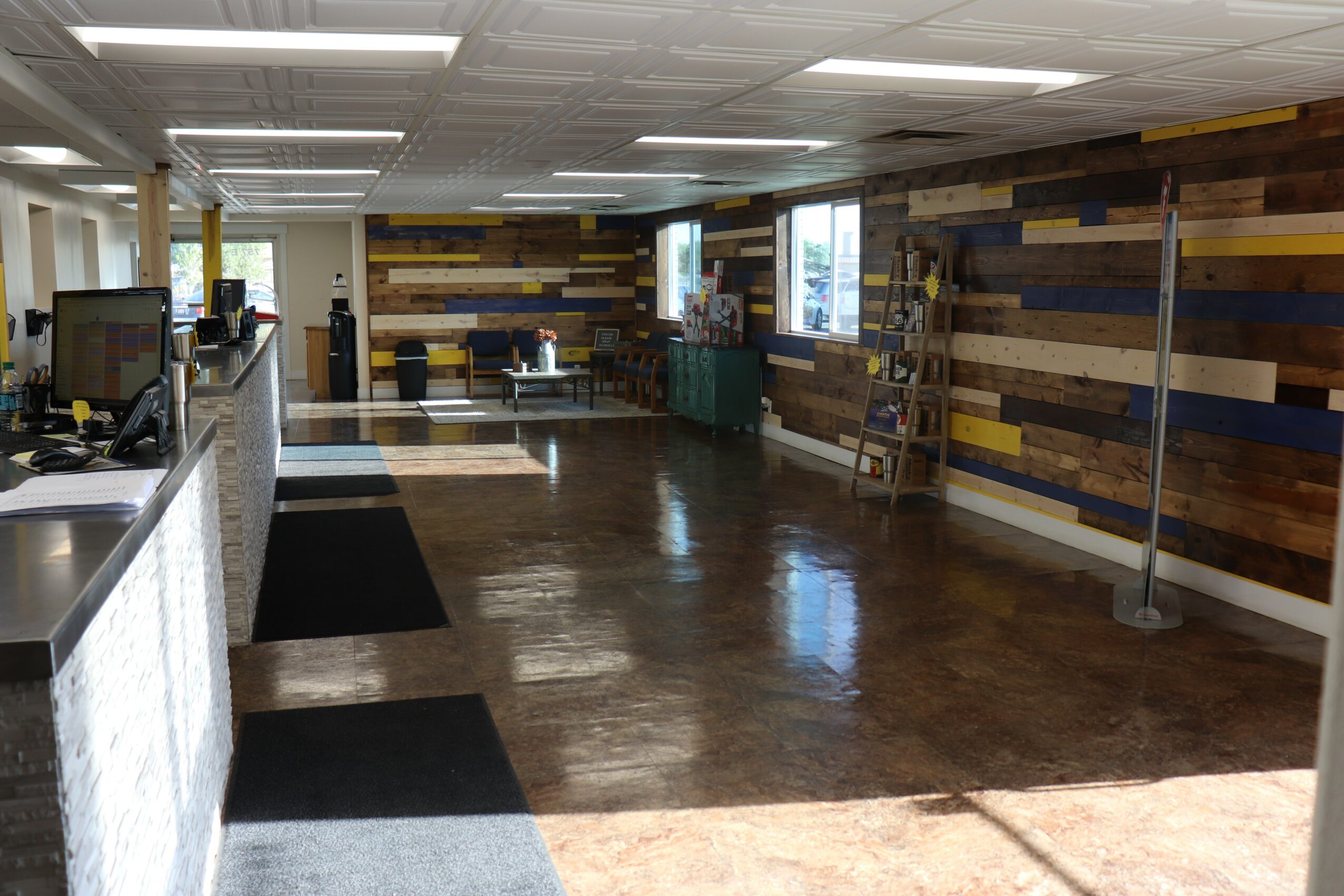 Interior space with wooden wall, windows, and polished floor, featuring a ladder and some furniture in the background.