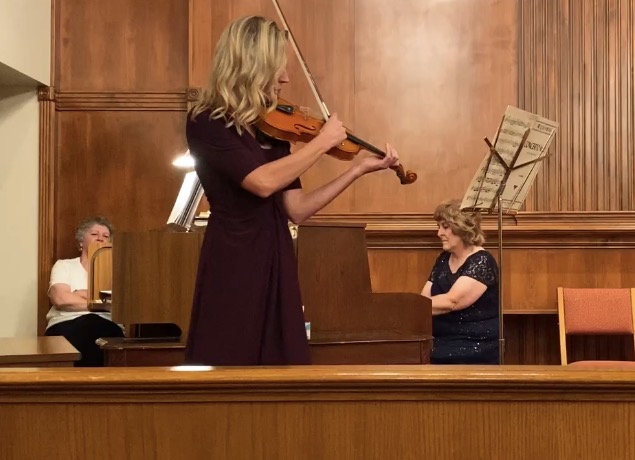 Woman playing violin in a room with a person sitting at a piano and sheet music on a stand.