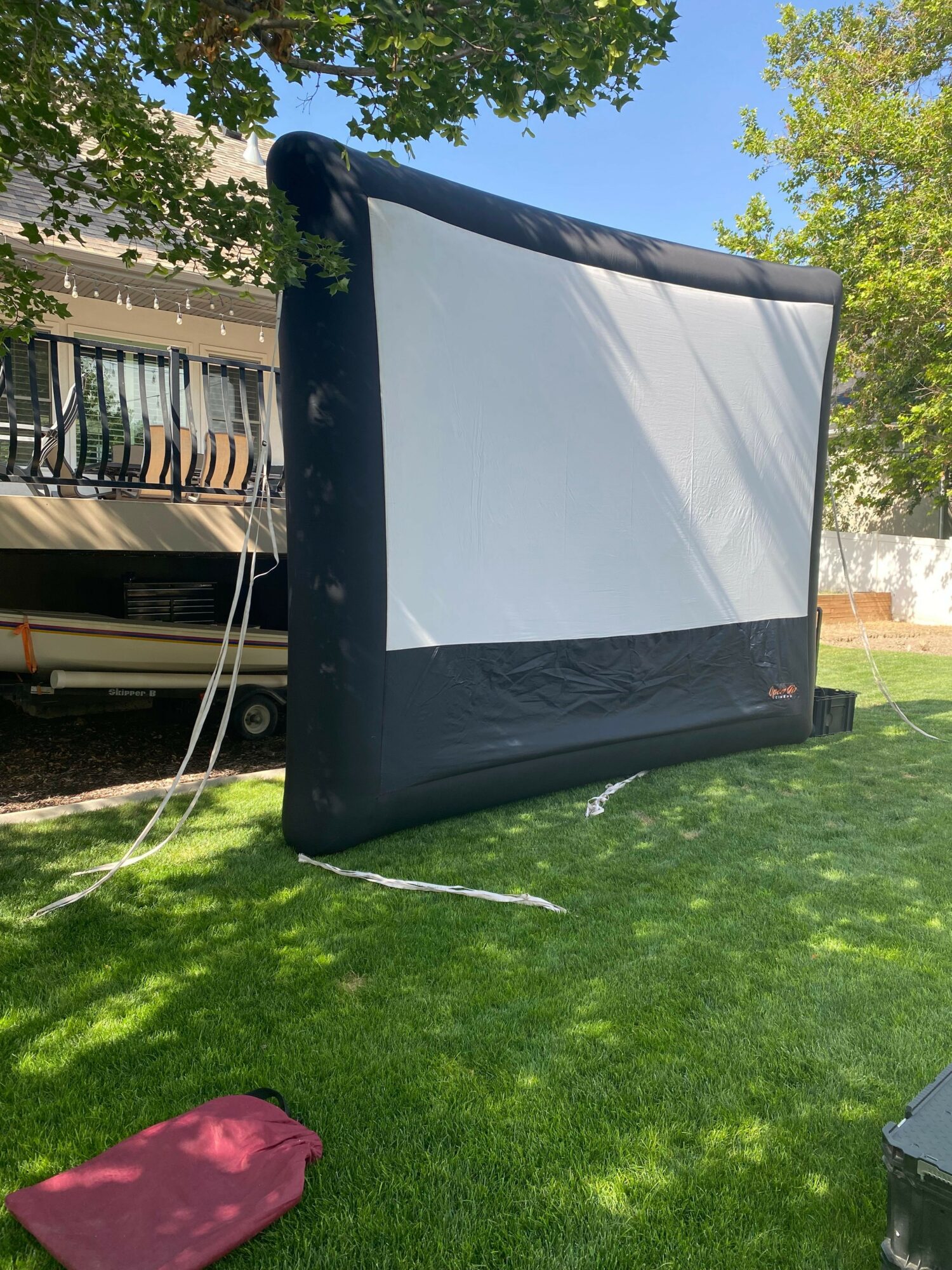 Inflatable outdoor movie screen set up on a grassy area with trees and a house in the background.