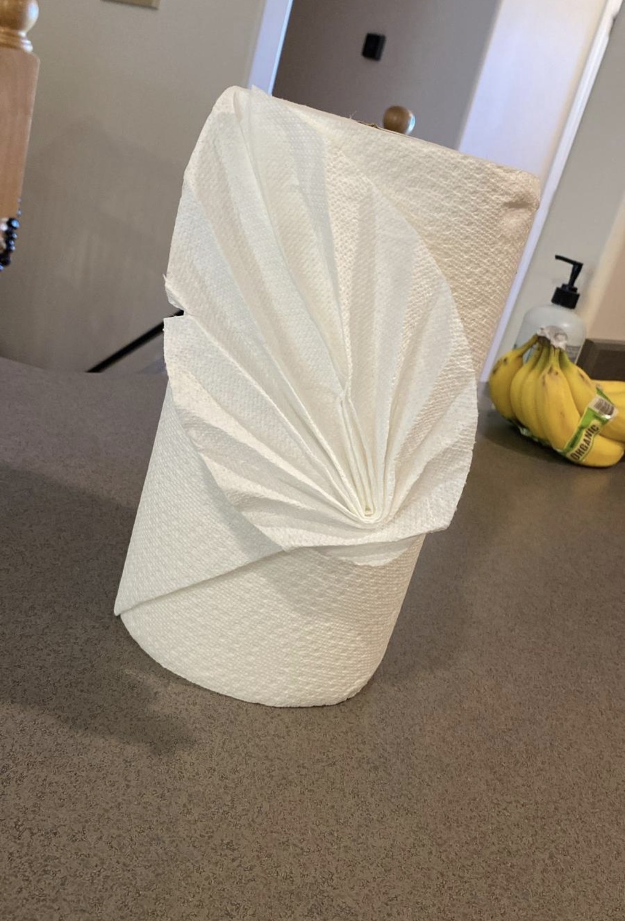 A roll of paper towels with a decorative paper napkin partially unfolded on top, placed on a dark countertop.