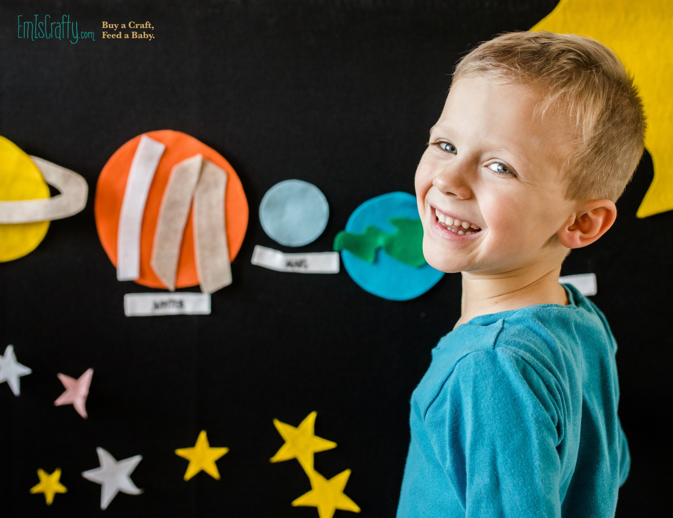 Smiling boy with short hair in a blue shirt in front of a space-themed display with paper planets and stars.