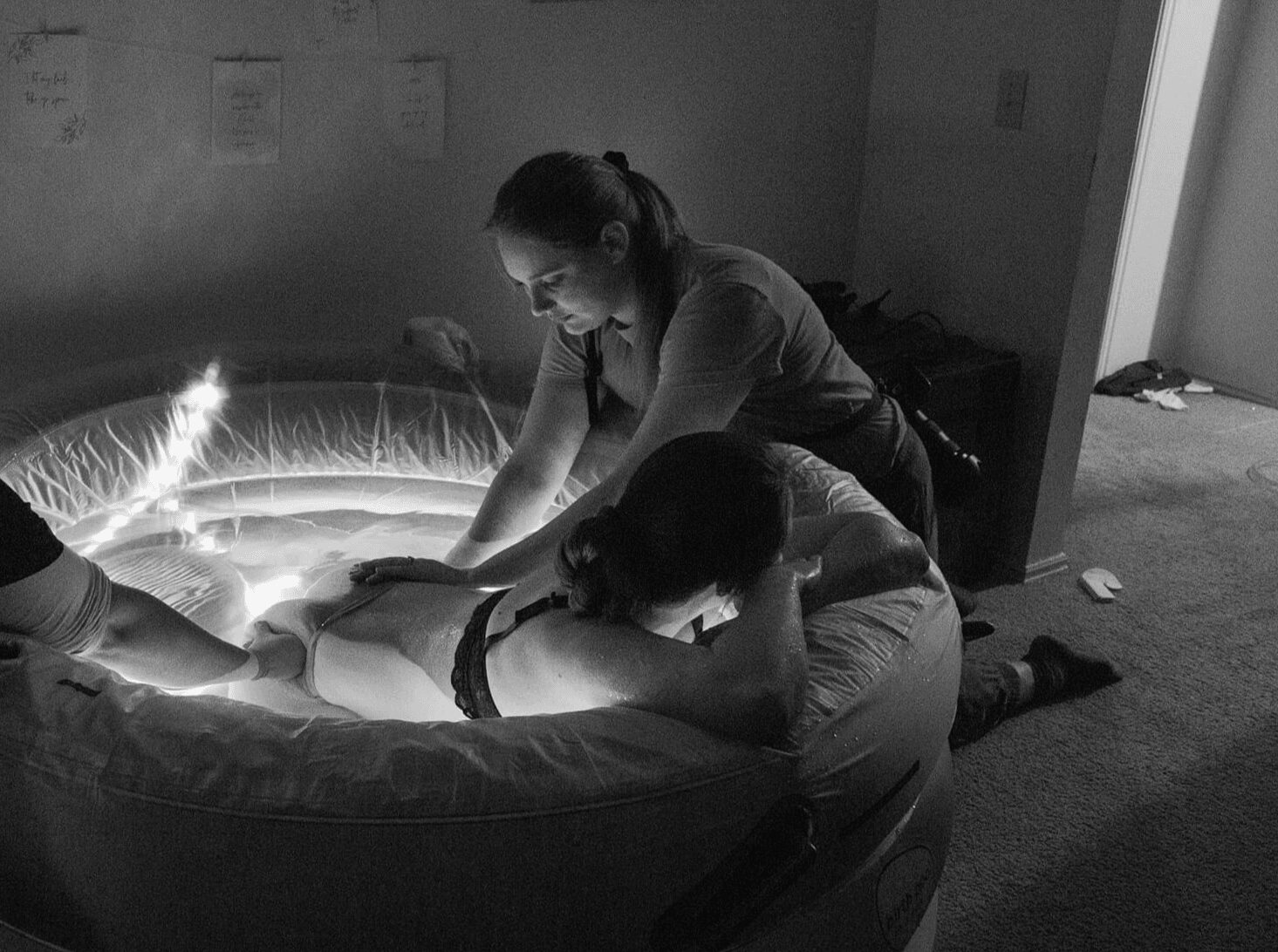 Woman leaning over a person lying in a circular illuminated medical or therapeutic device in a dim room.
