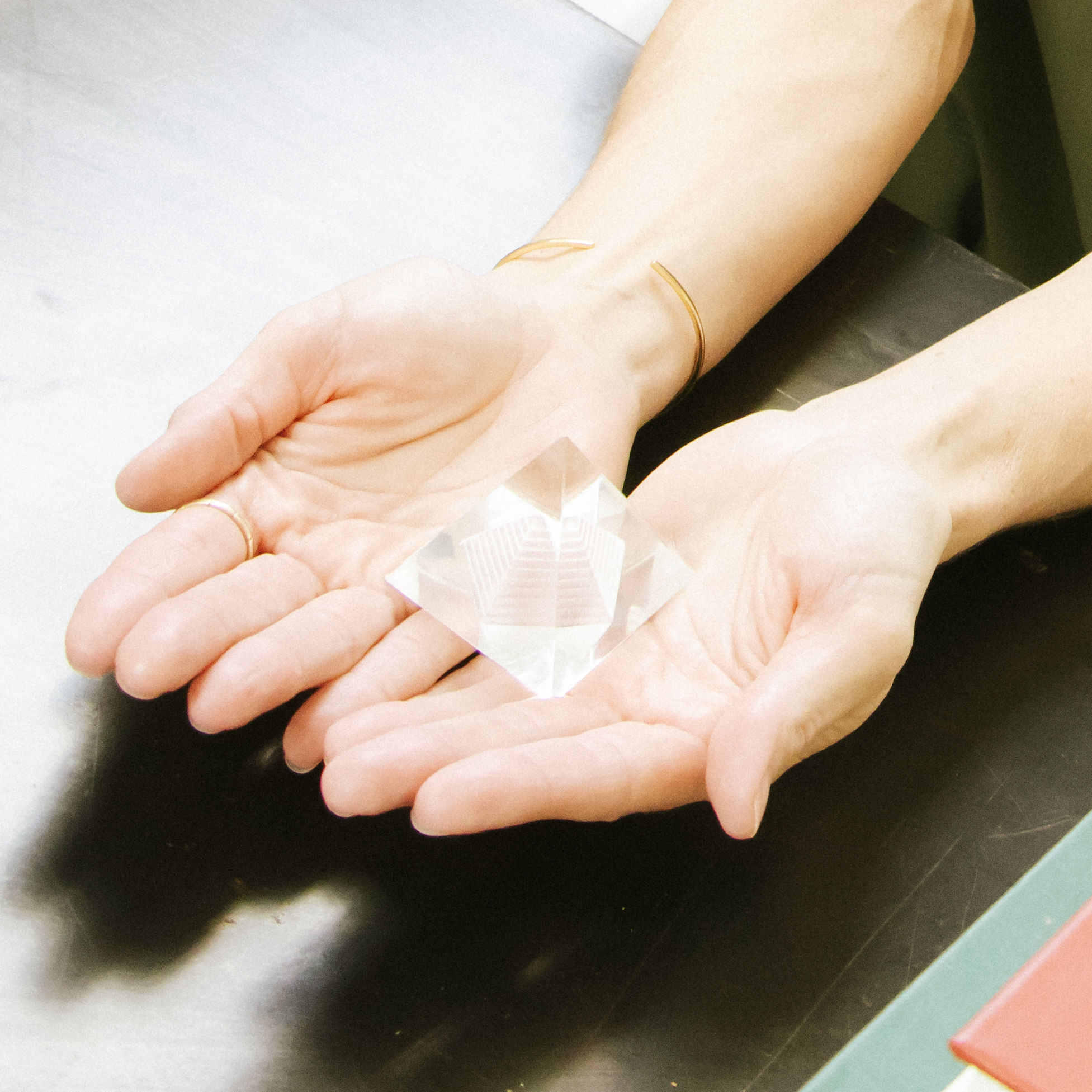 Person holding a clear, faceted gemstone in their hands over a dark surface.