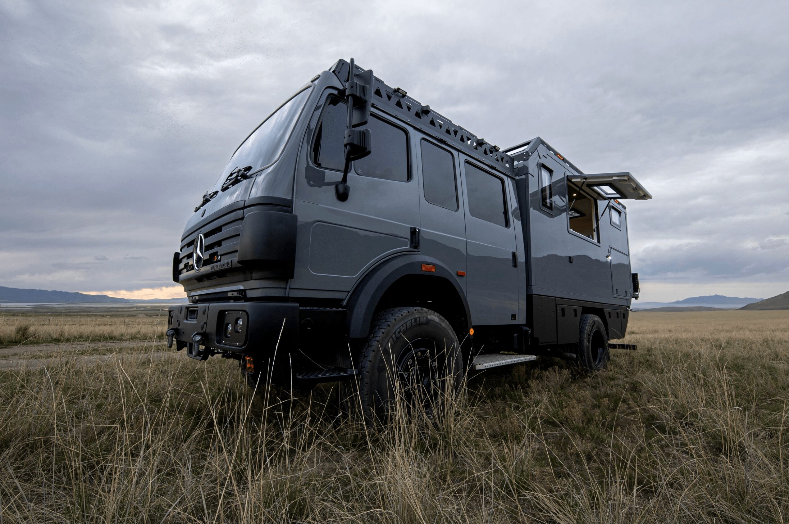 Large gray off-road vehicle with extended equipment on a grassy plain under cloudy sky