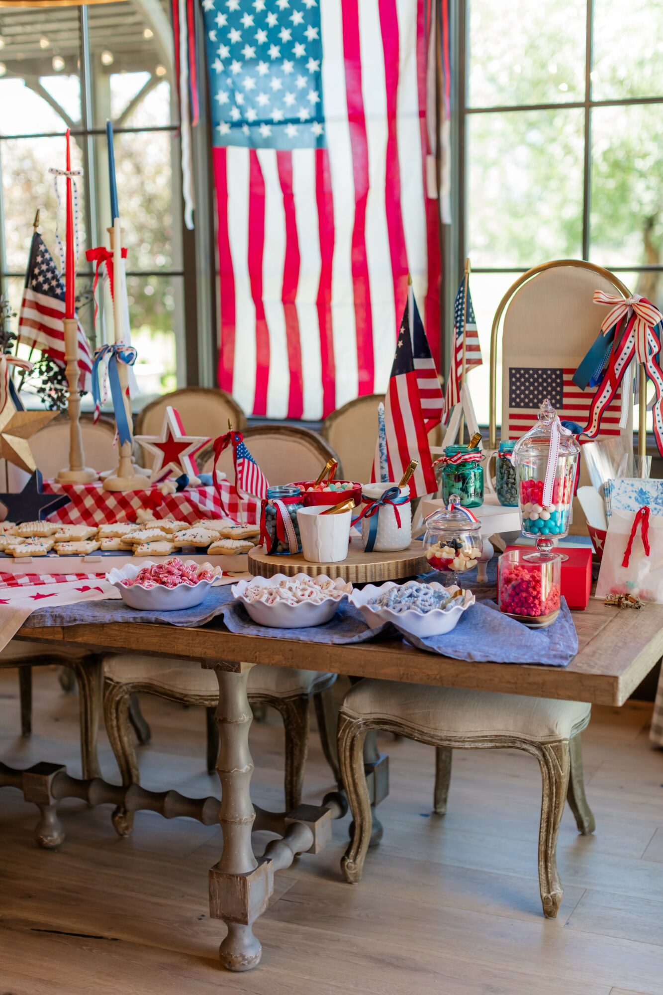 Table decorated with American flags, patriotic-themed items, and red, white, and blue decorations, with a large American flag hanging in the background.