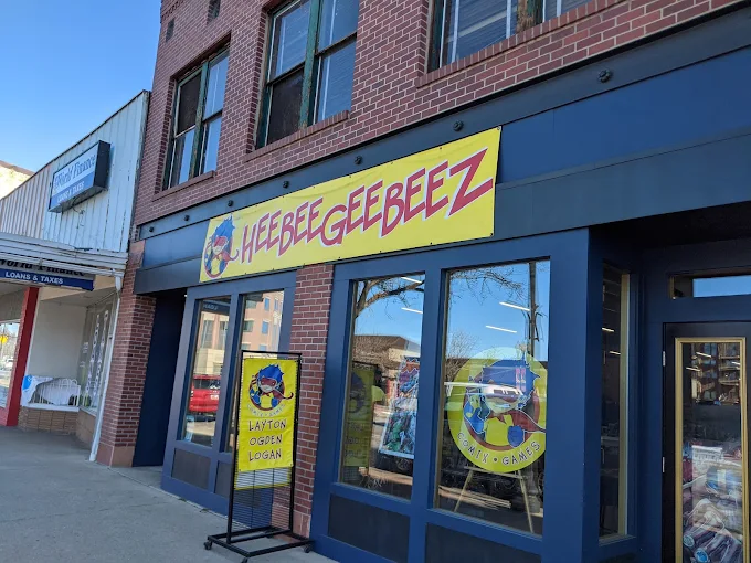Storefront with a yellow sign displaying text and a logo, large windows reflecting the street, and a sidewalk in front.