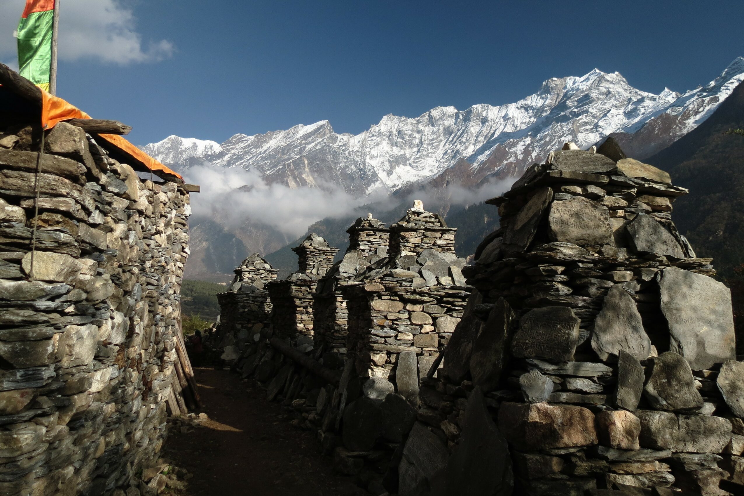 Stone structures with snow-capped mountains in the background under a blue sky.