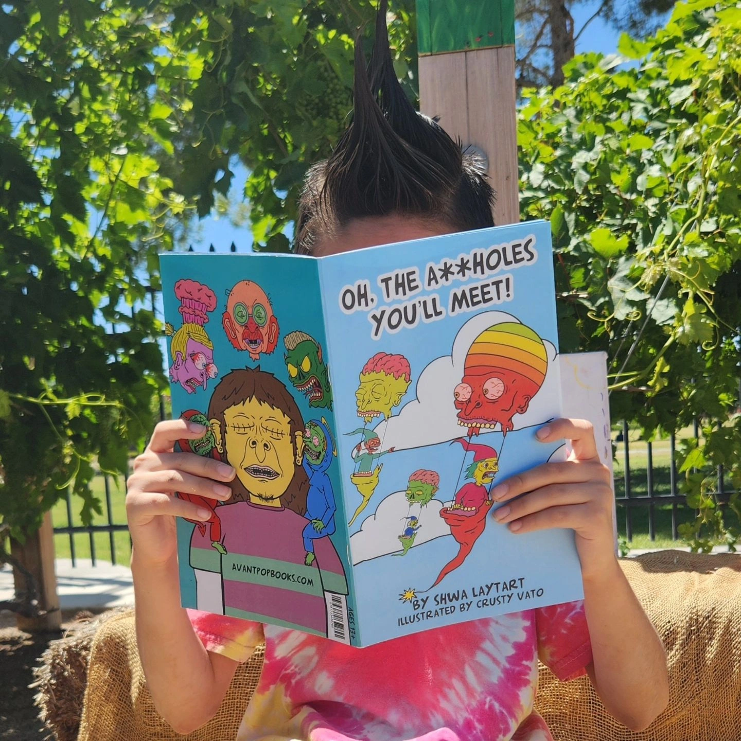 Child with spiked hair reading a colorful comic book outdoors, surrounded by green trees and sunlight.