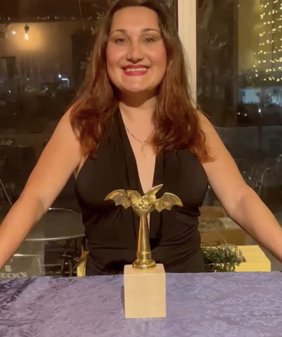 Woman with shoulder-length hair smiling at a table with a golden trophy in front of her.