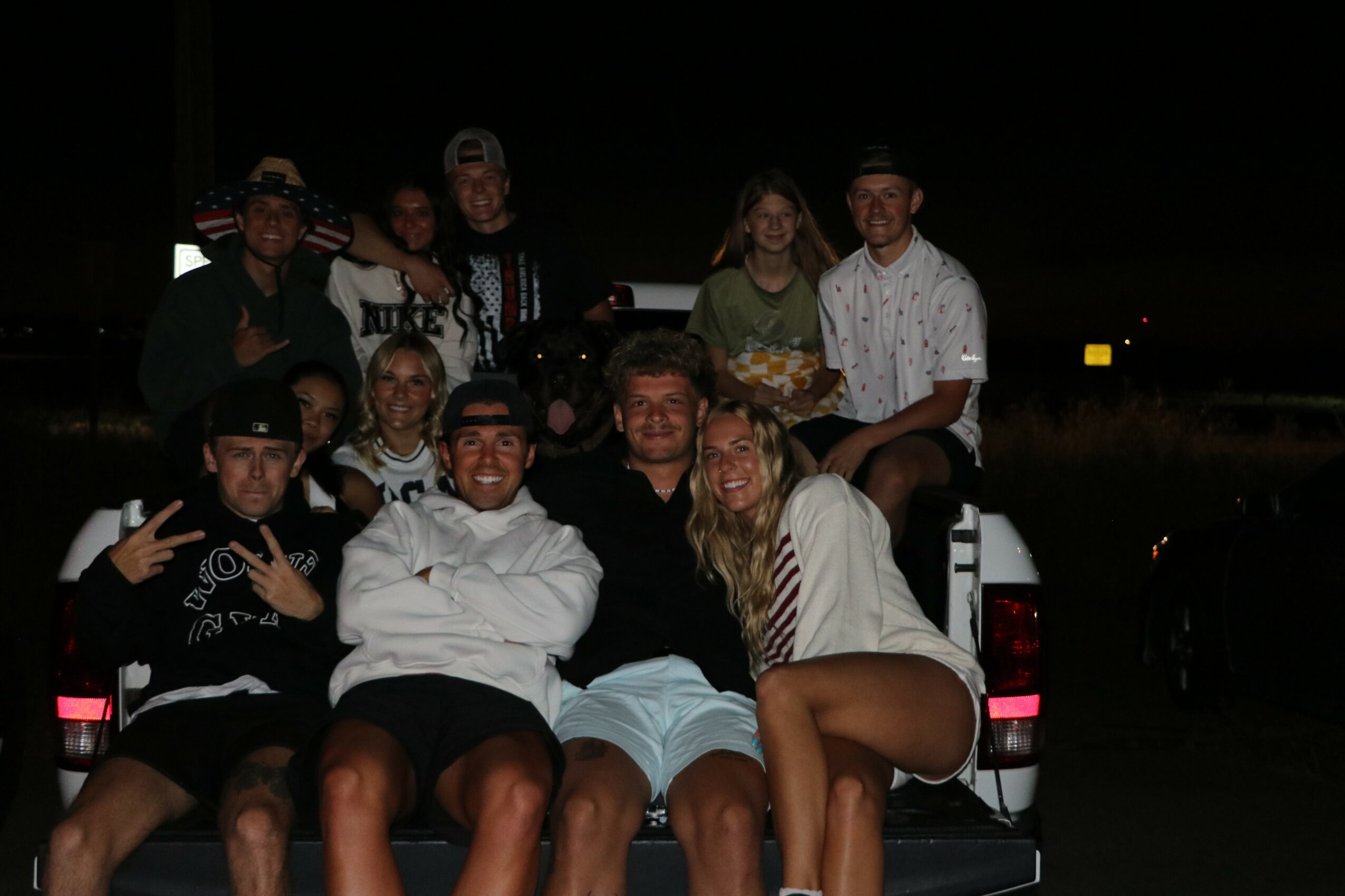 Group of ten people sitting and standing around a vehicle at night, some smiling and making gestures.