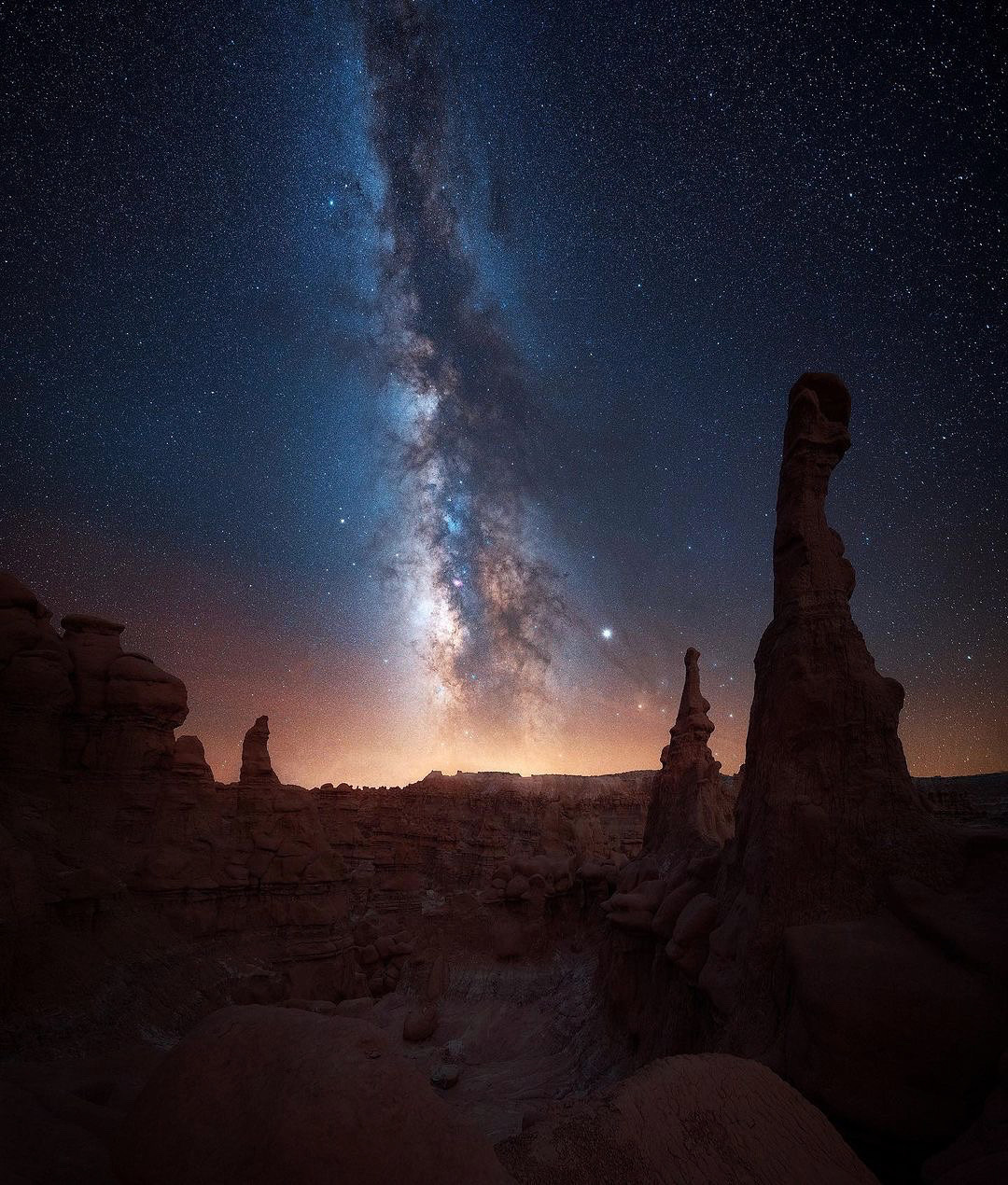 Night sky with the Milky Way galaxy over a desert landscape with rock formations, stars visible in the sky.
