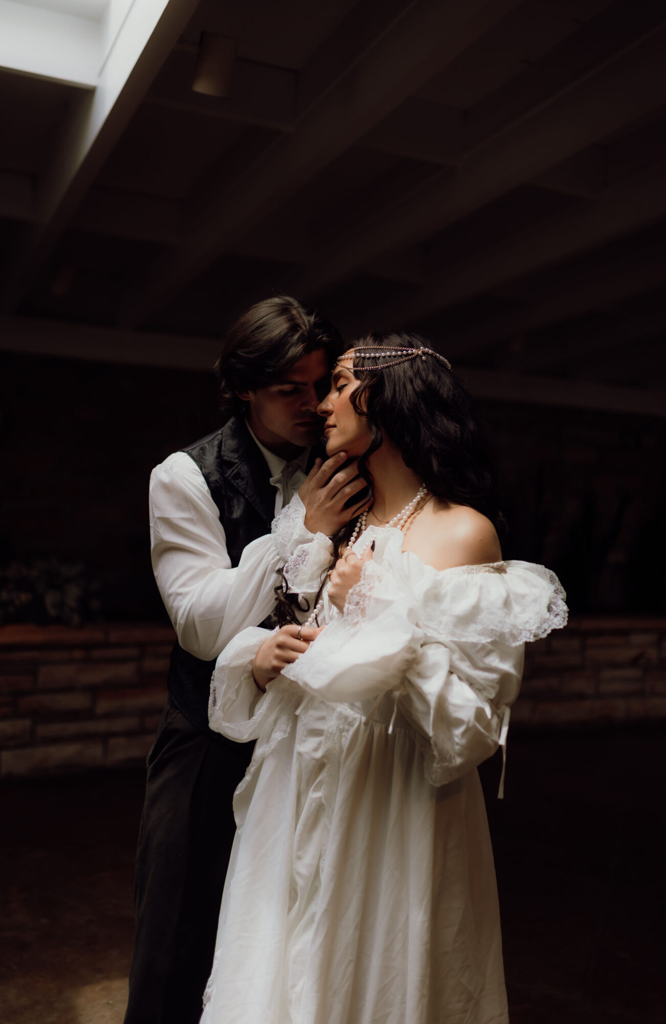 Two people in formal attire close together, under a dark ceiling, with one touching the other's face.