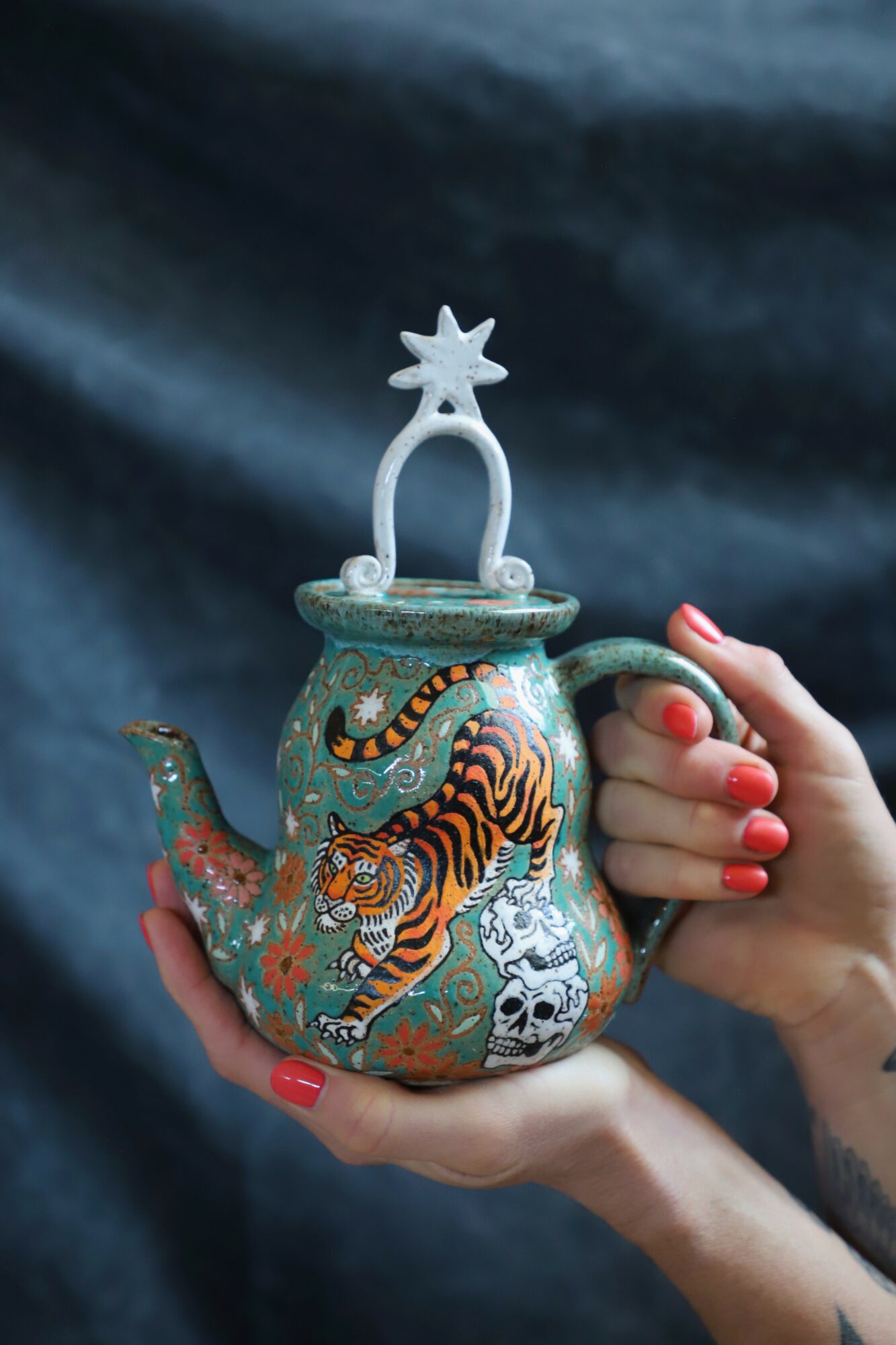 Person holding a decorative teapot with a tiger design and a star-shaped handle, against a dark background.