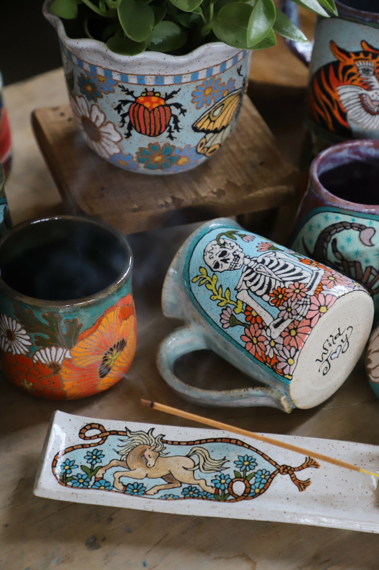 Decorative painted cups and a ceramic tray with floral and animal designs on a wooden surface.