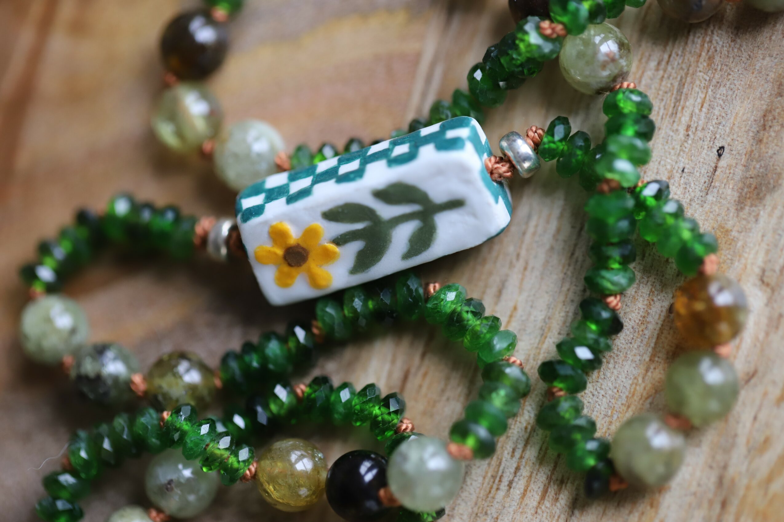 Multiple beaded bracelets with green, white, and yellow beads, and a fabric bead with a floral design, on a wooden surface.