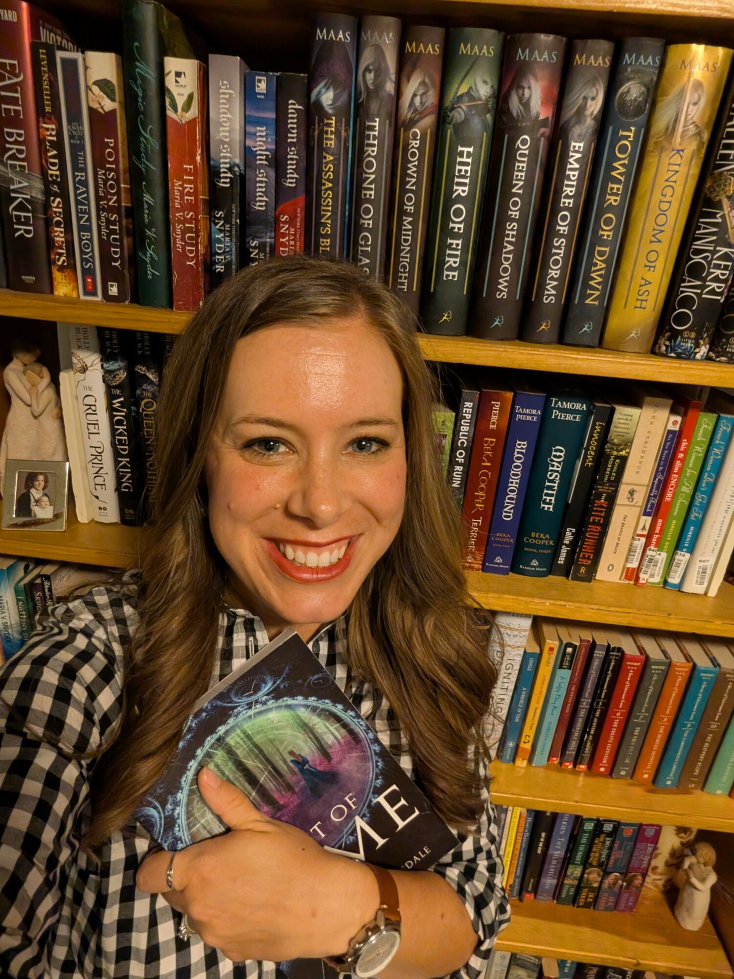 Woman smiling holding a book in front of bookshelves filled with various books.