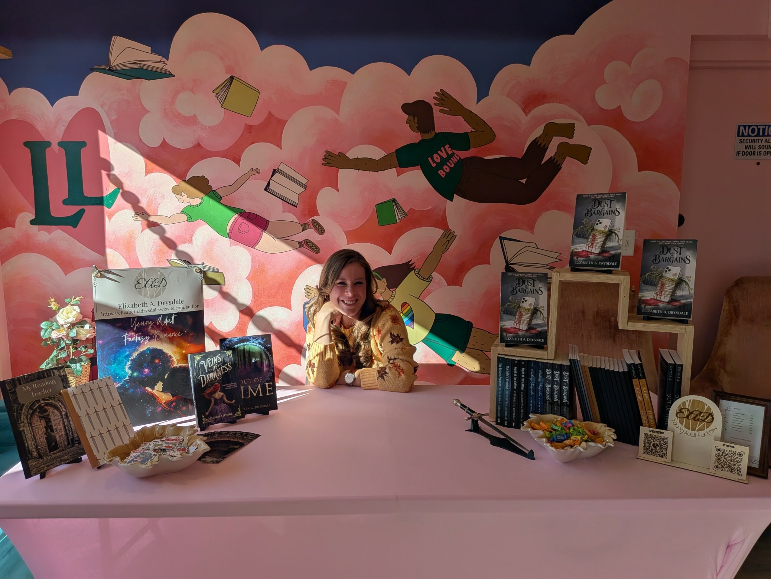 Girl sitting at a table with books and decorations, colorful cloud mural with a flying person in the background.