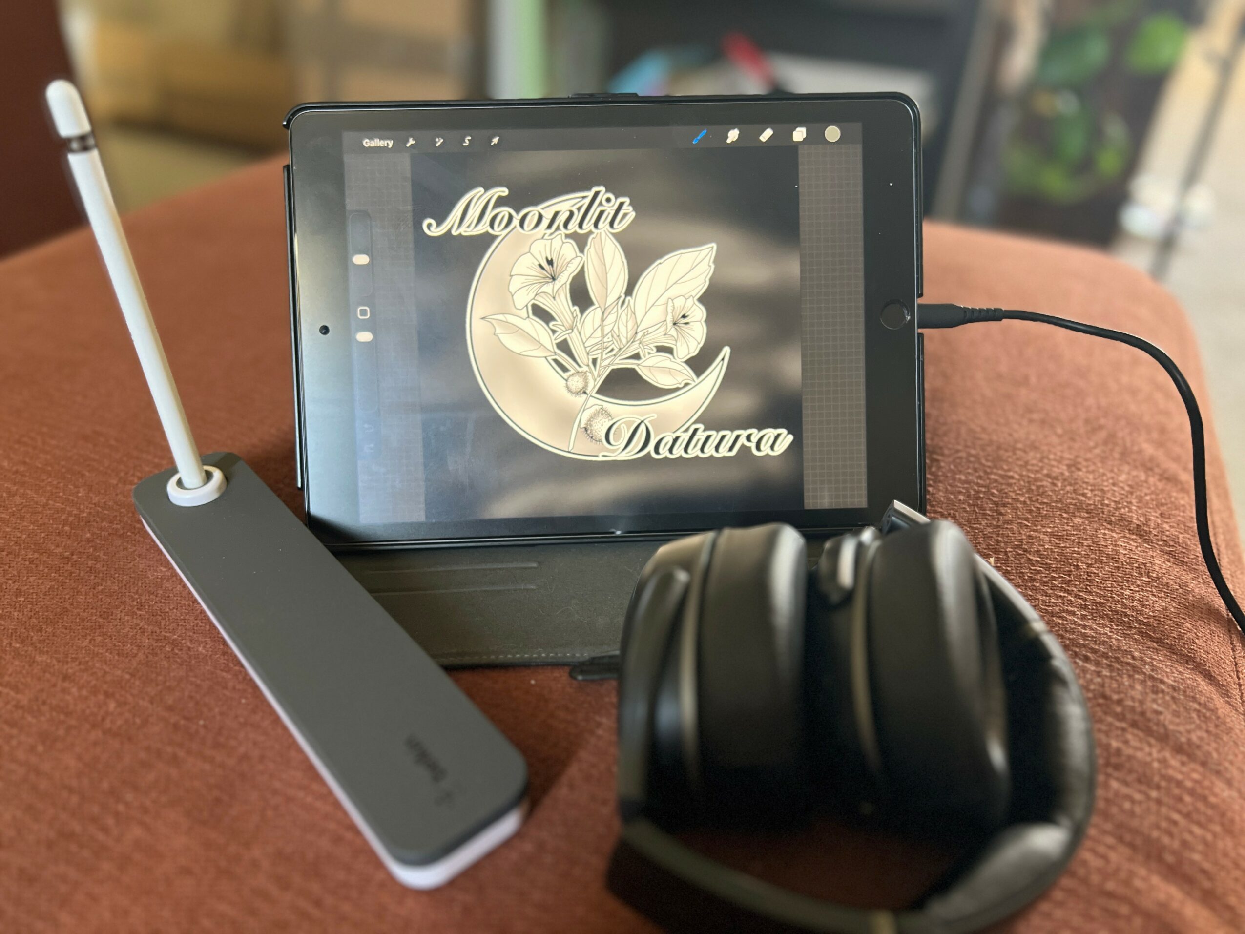 Tablet displaying a logo with a butterfly and text, connected to a device with a stylus, and black headphones on a brown surface.