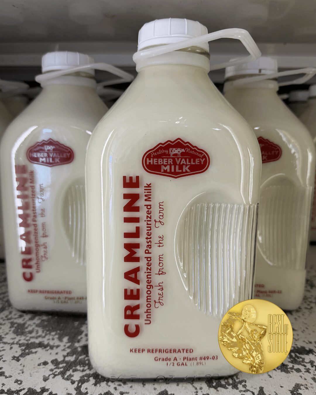 Cream Valley milk bottle with a red label, a gold medal, and a white cap, on a store shelf.
