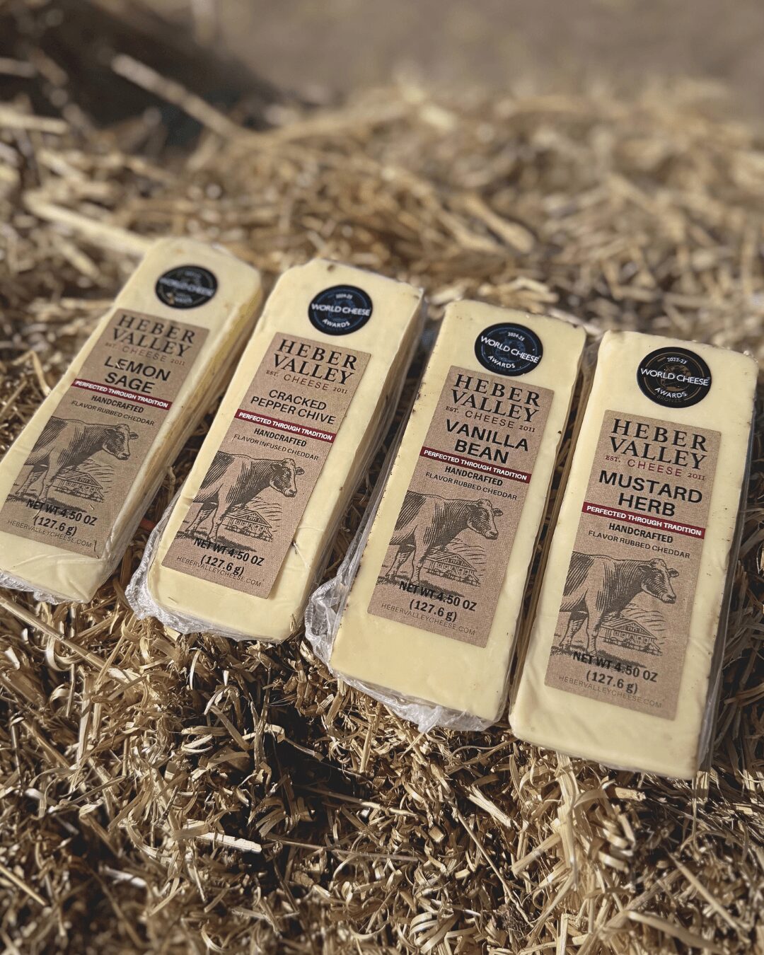 Four blocks of herbal soap with vintage-style labels, placed on dry grass outdoors.