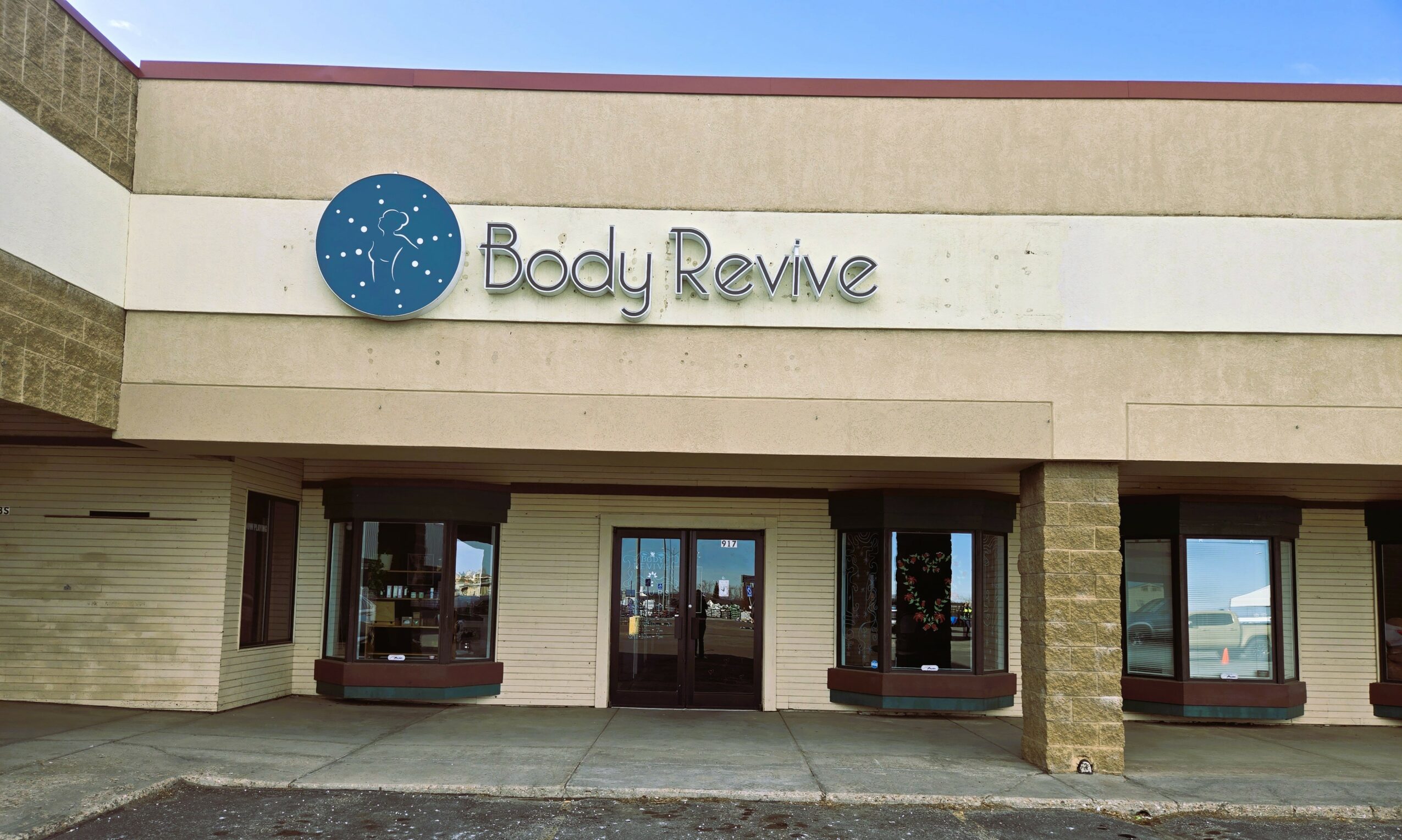 Storefront with a sign reading 'Body Revive' and a blue logo, three windows, and a door in the center.