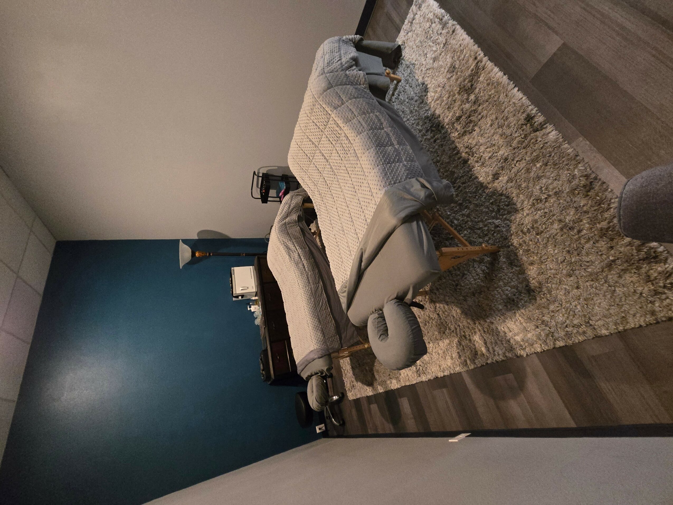Bedroom with bed, nightstand, and a blue accent wall, viewed from the side, with a rug on the floor.