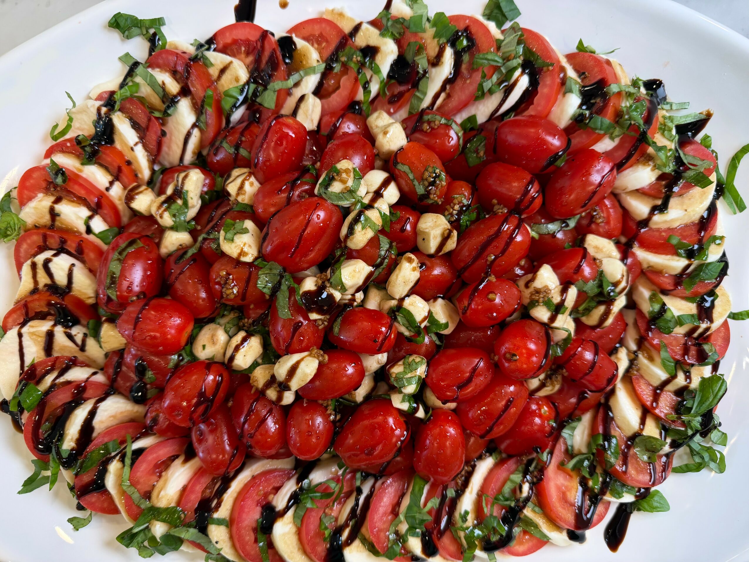 A colorful salad with cherry tomatoes, sliced radishes, chopped herbs, and drizzled dressing on a white plate.
