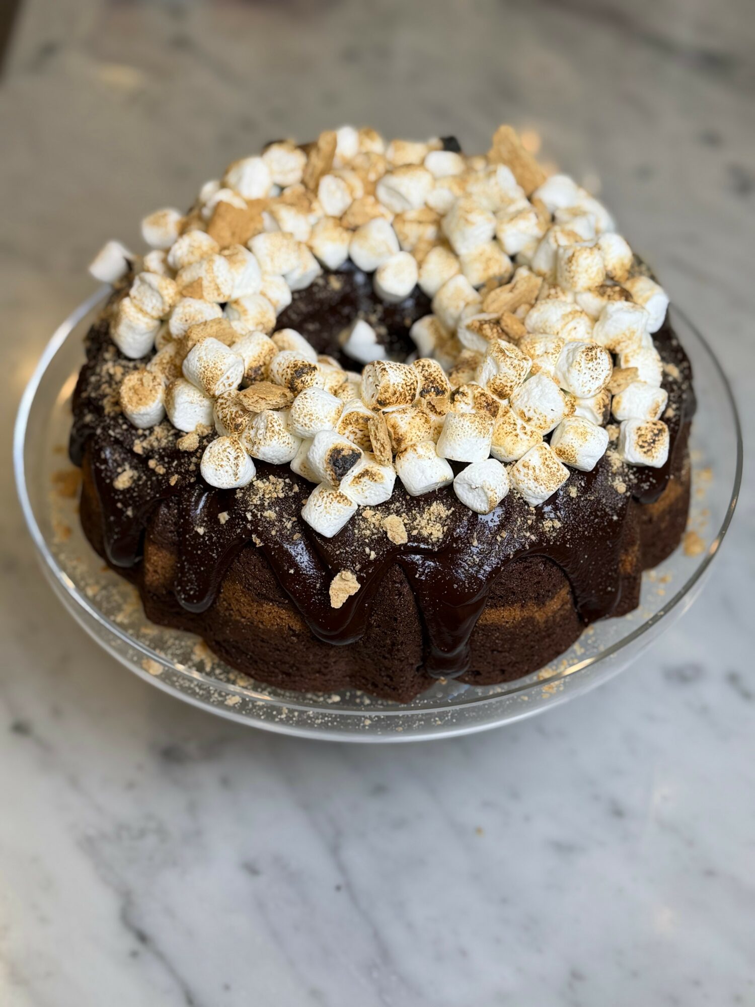 Chocolate cake topped with toasted marshmallows on a glass plate, with a marble surface background.