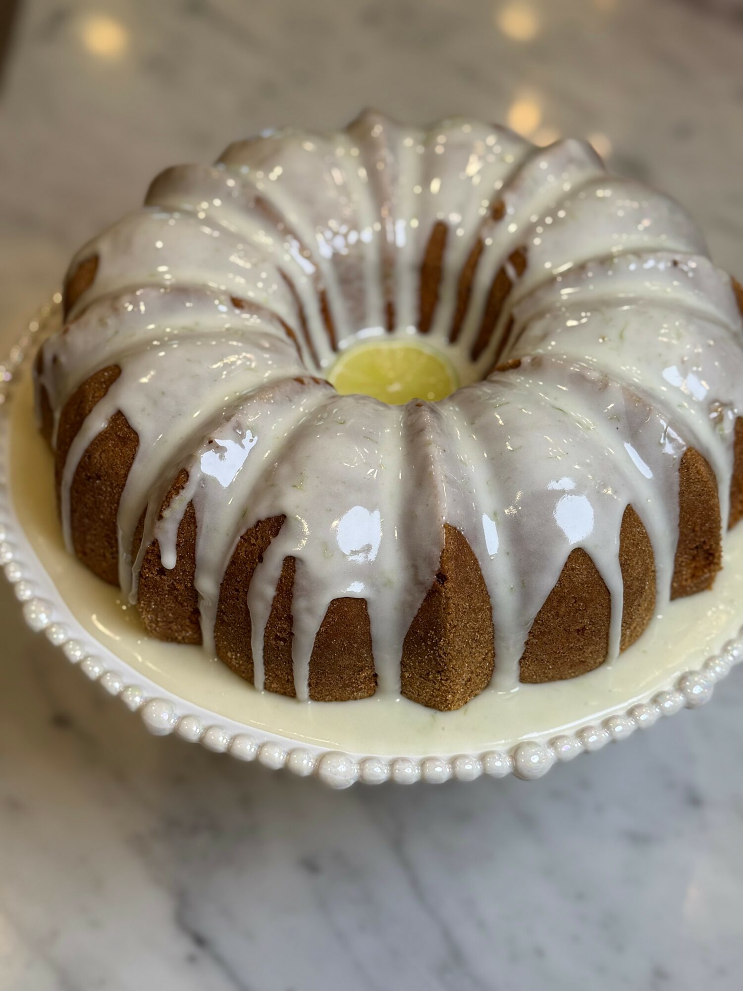 Bundt cake with white glaze and a yellow center on a decorative plate, marble surface background.