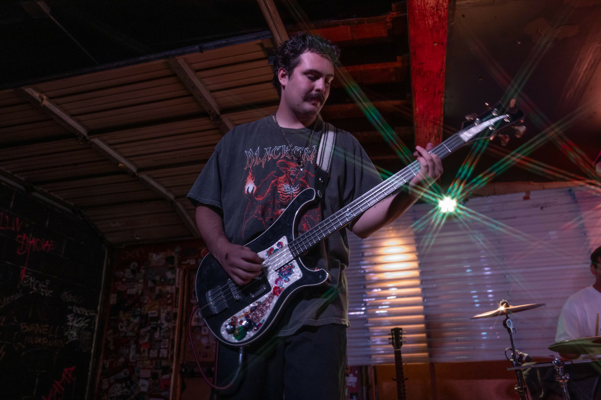 Person playing electric guitar on stage with colorful lights and wooden background.