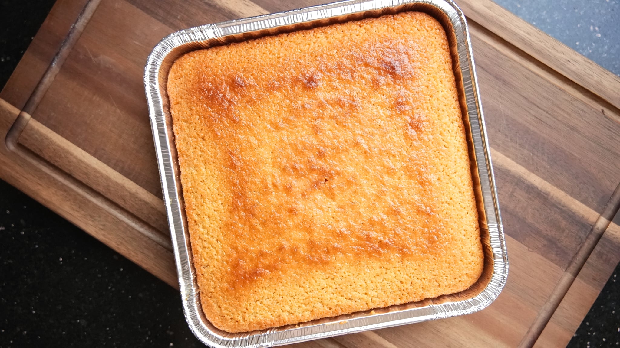 Baked square cake in a metal pan on a wooden surface.