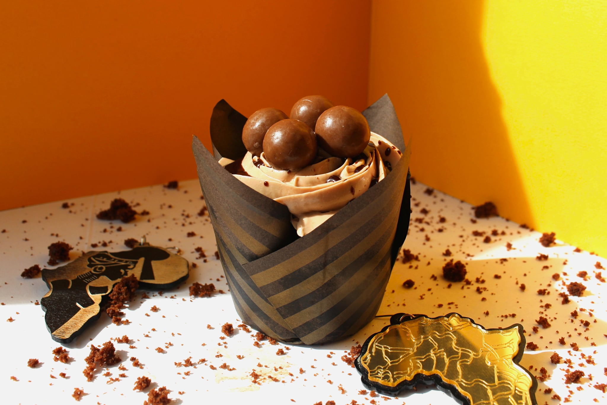 Cup with chocolate balls and cream, on a white surface with scattered crumbs and chocolate pieces, yellow background.