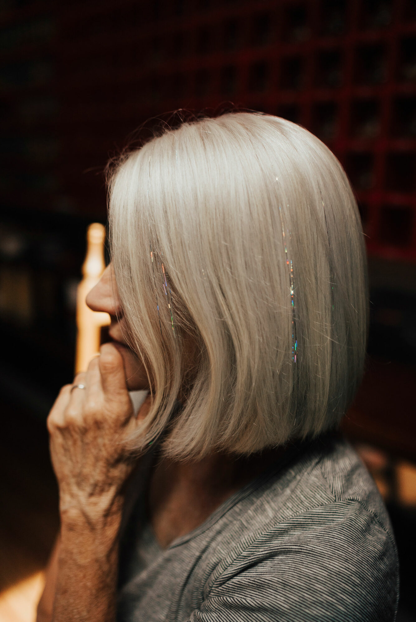 Side view of an elderly woman with straight, silver hair, wearing a gray top, touching her face with her hand.