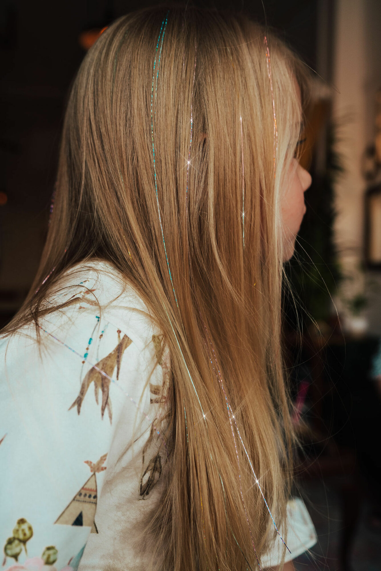 Side view of a person with long, straight blonde hair, wearing a white top with colorful patterns.