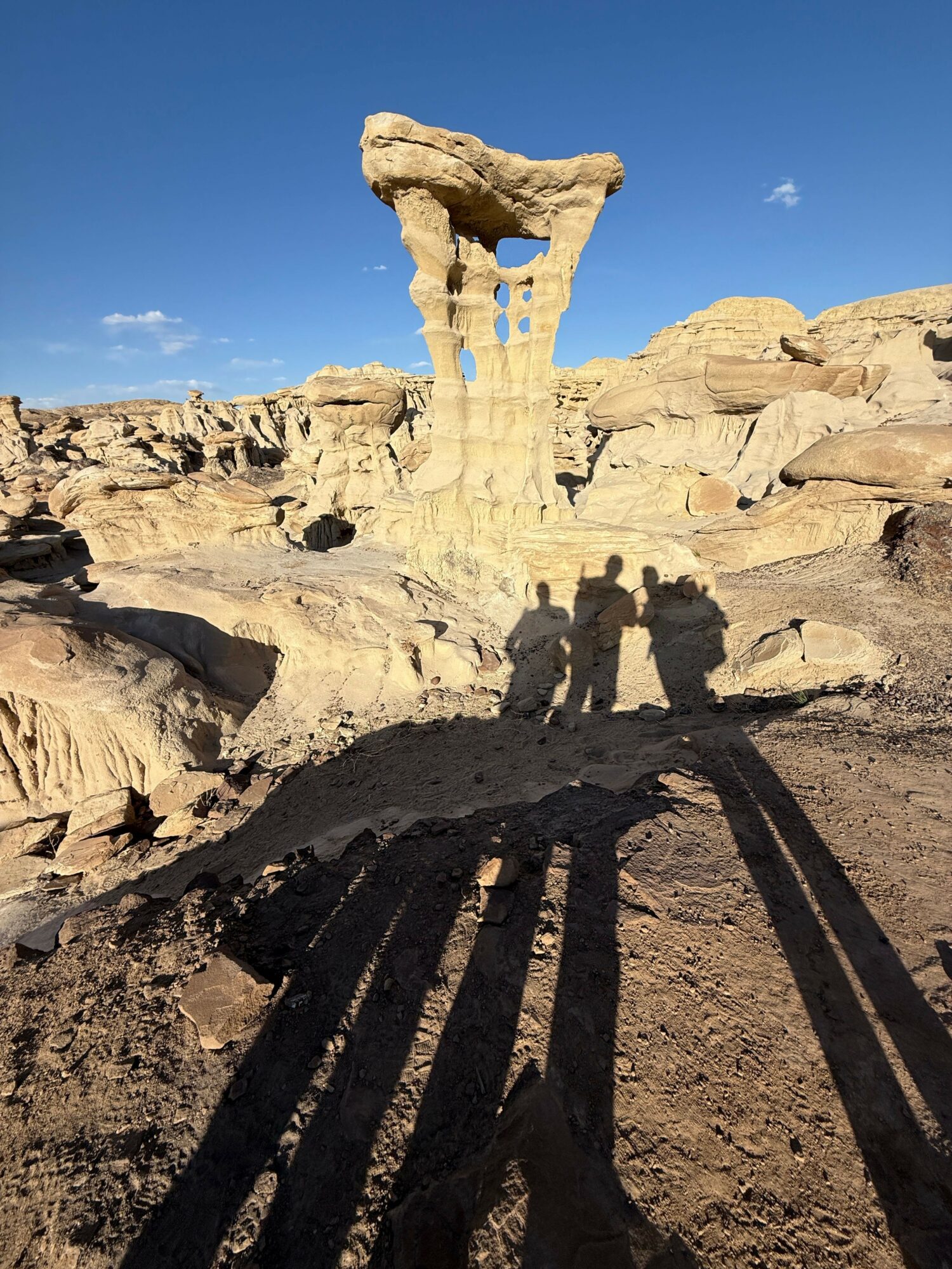 Rock formations with shadows cast on sandy ground under a clear blue sky.