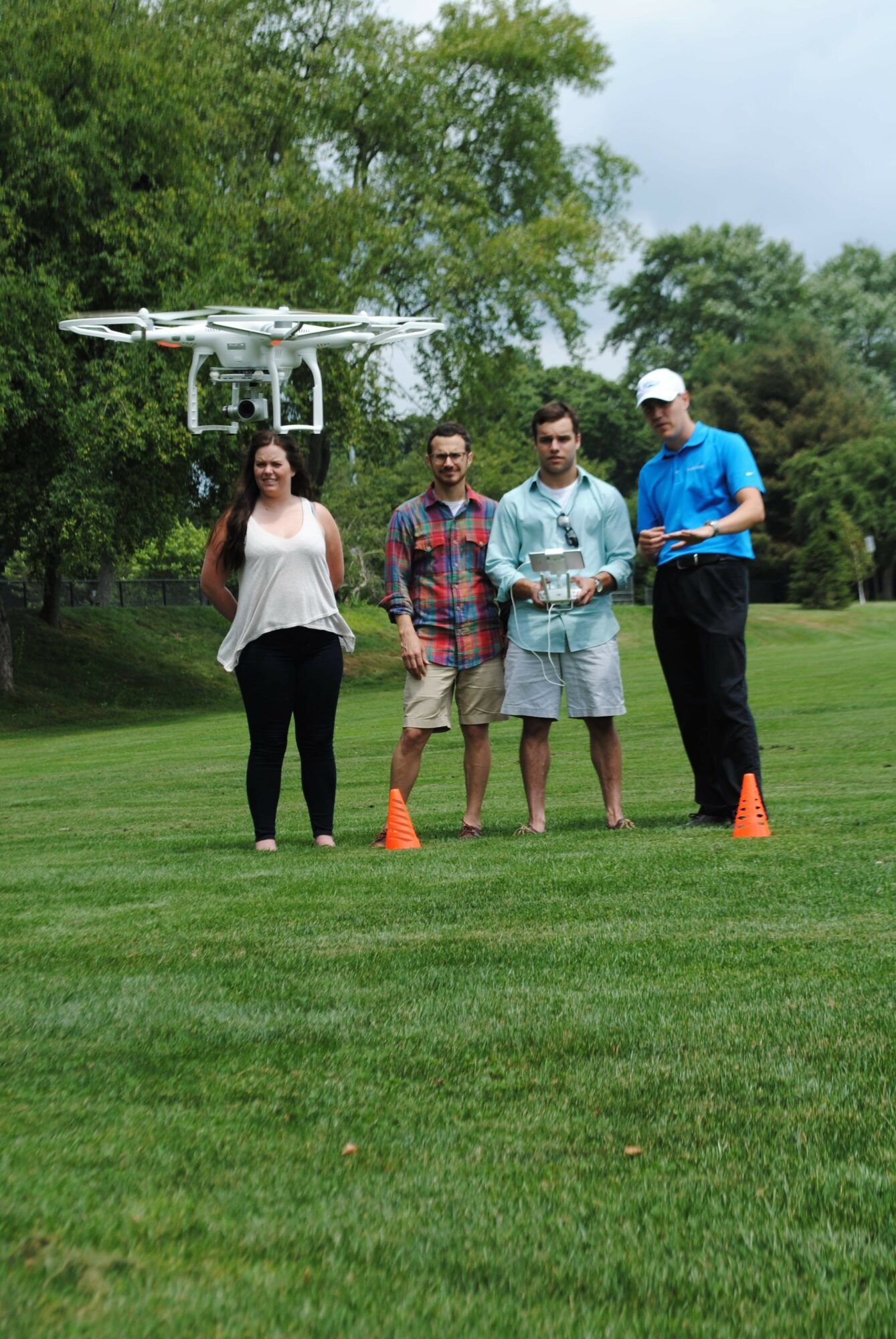 Four people standing on grass near a white structure with trees in the background.
