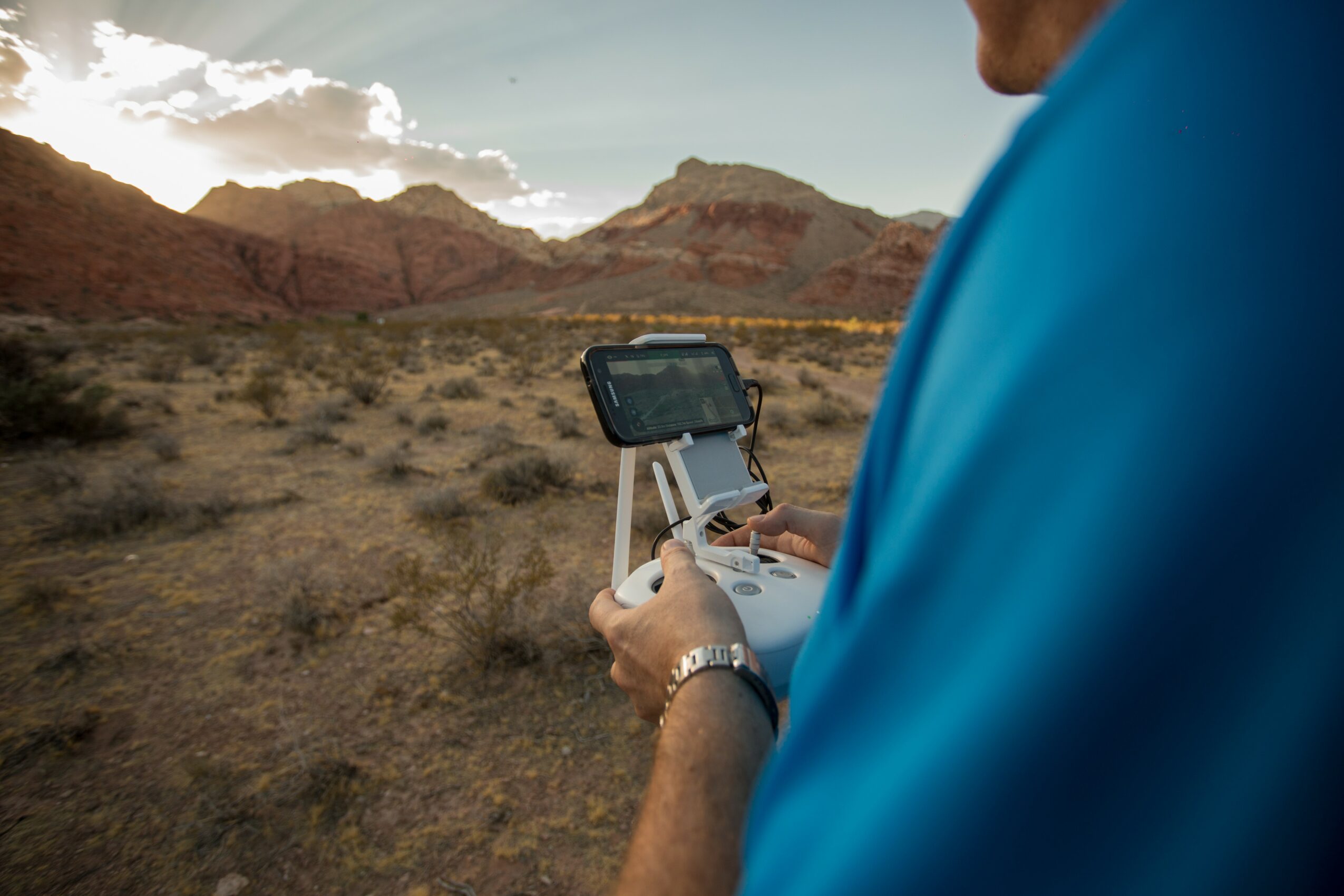 Person holding a drone controller outdoors in a desert landscape with mountains and cloudy sky.