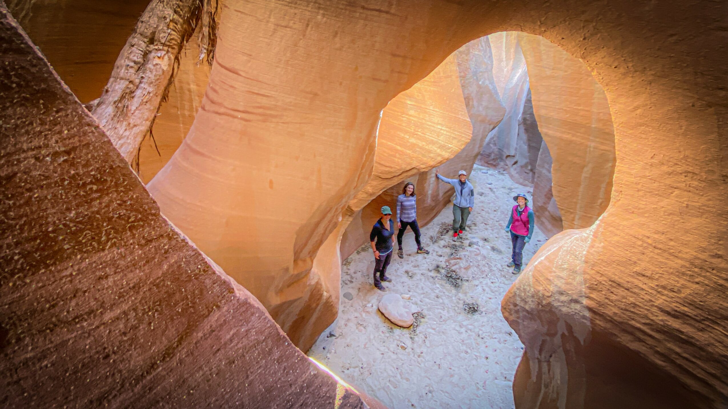 Group of people walking through a narrow canyon with smooth, curved rock walls and an arch-shaped opening.