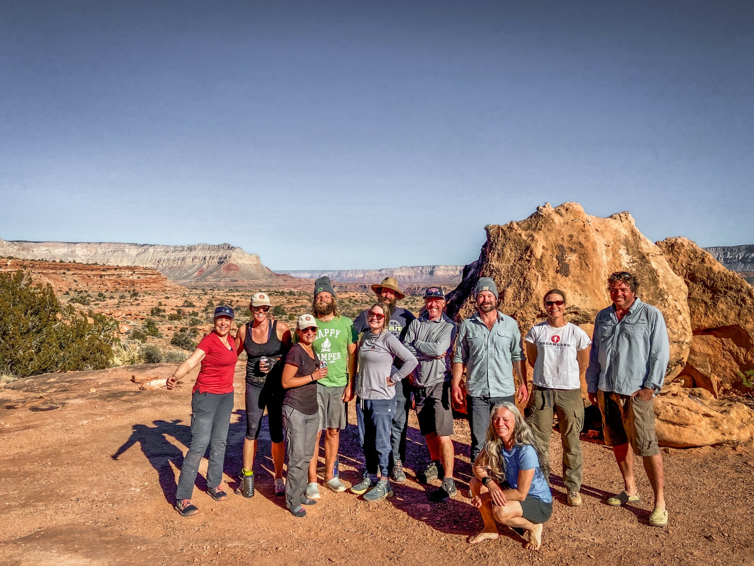 Group of people standing outdoors in a desert landscape with rock formations and clear sky.