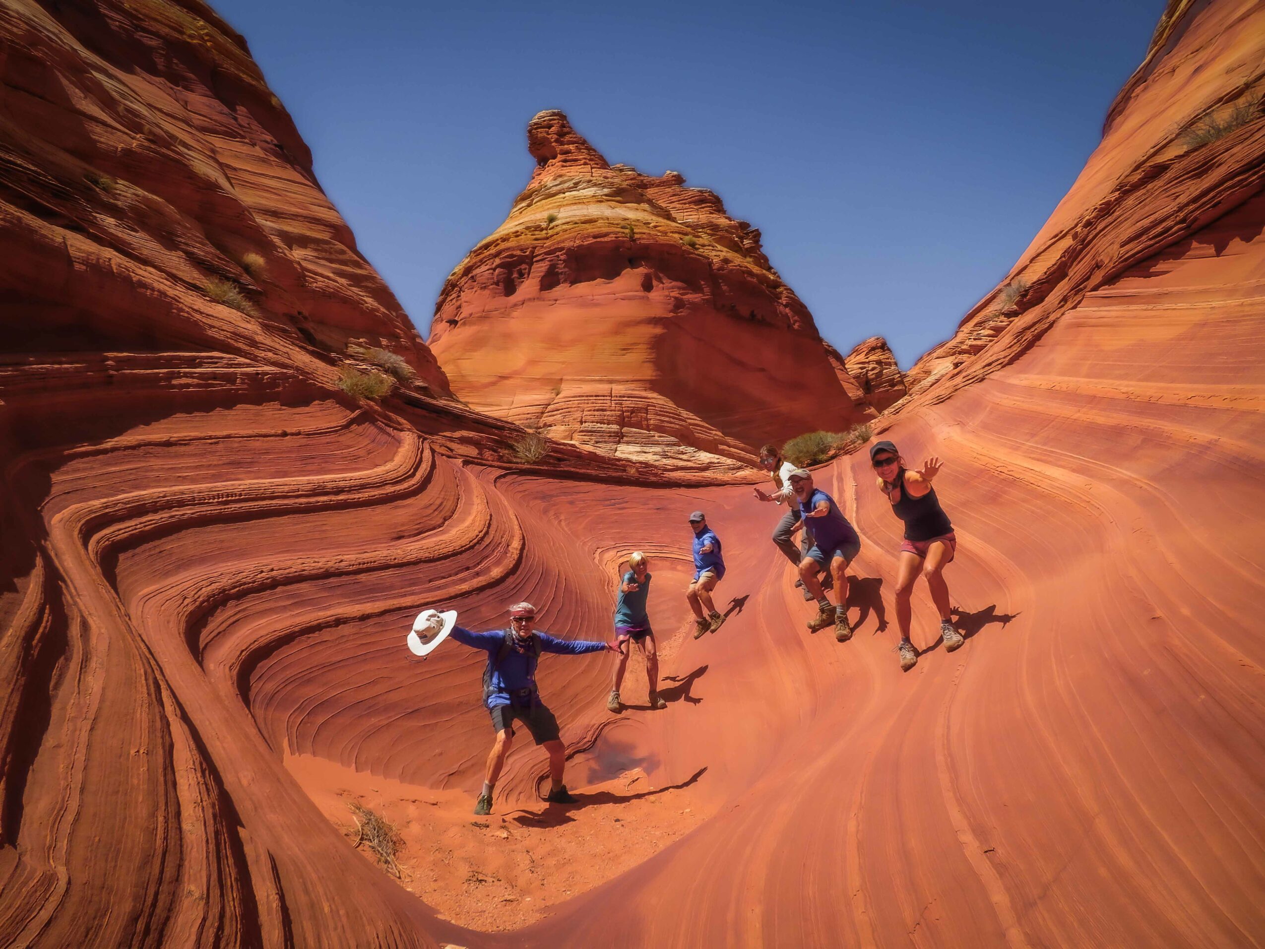 Group of people walking through a colorful, layered canyon with steep, curved walls and a blue sky above.