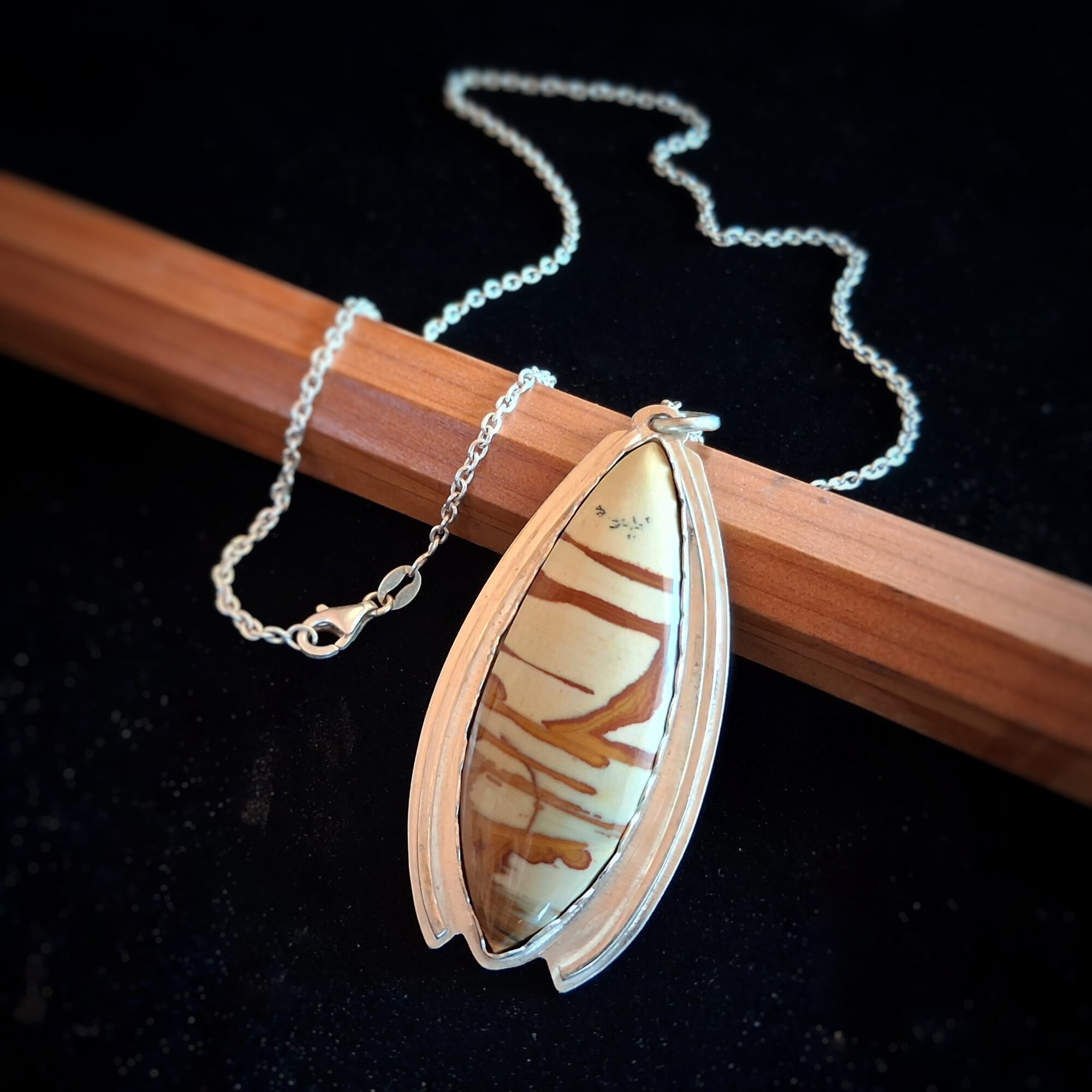 Pendant necklace with a large shell, chain, on a black background with a wooden piece.