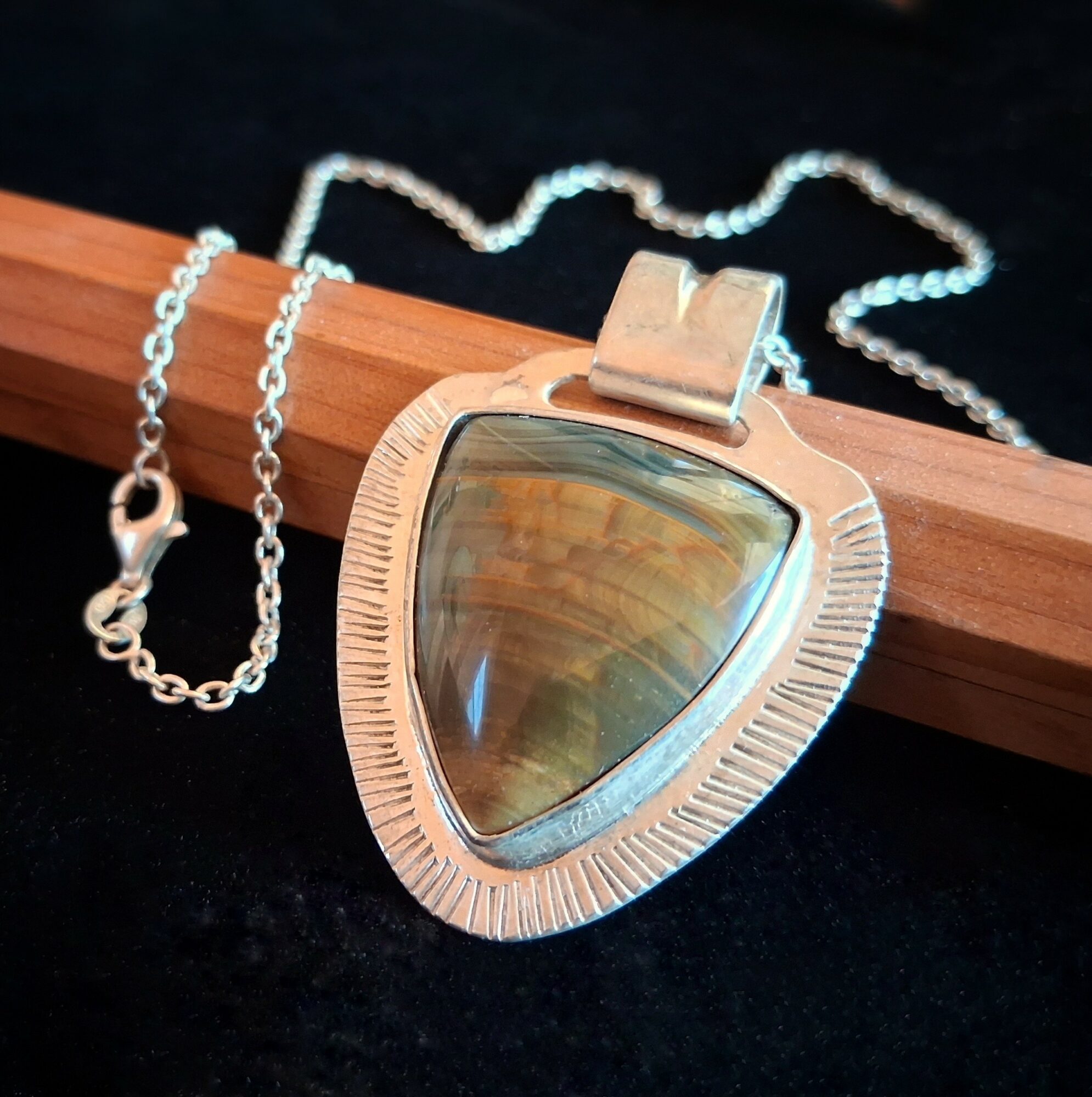 Silver necklace with a large triangular pendant featuring a polished, reflective stone, on a black background.