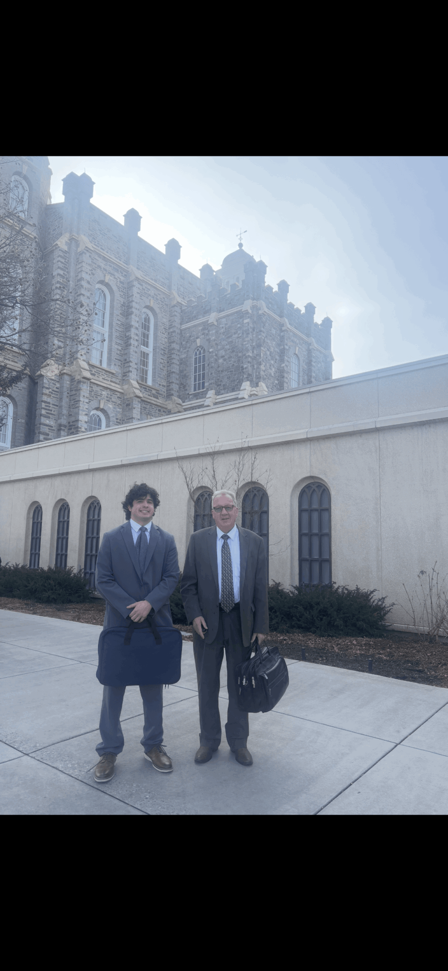 Two people in suits and masks standing outside a historic building with ornate architecture.