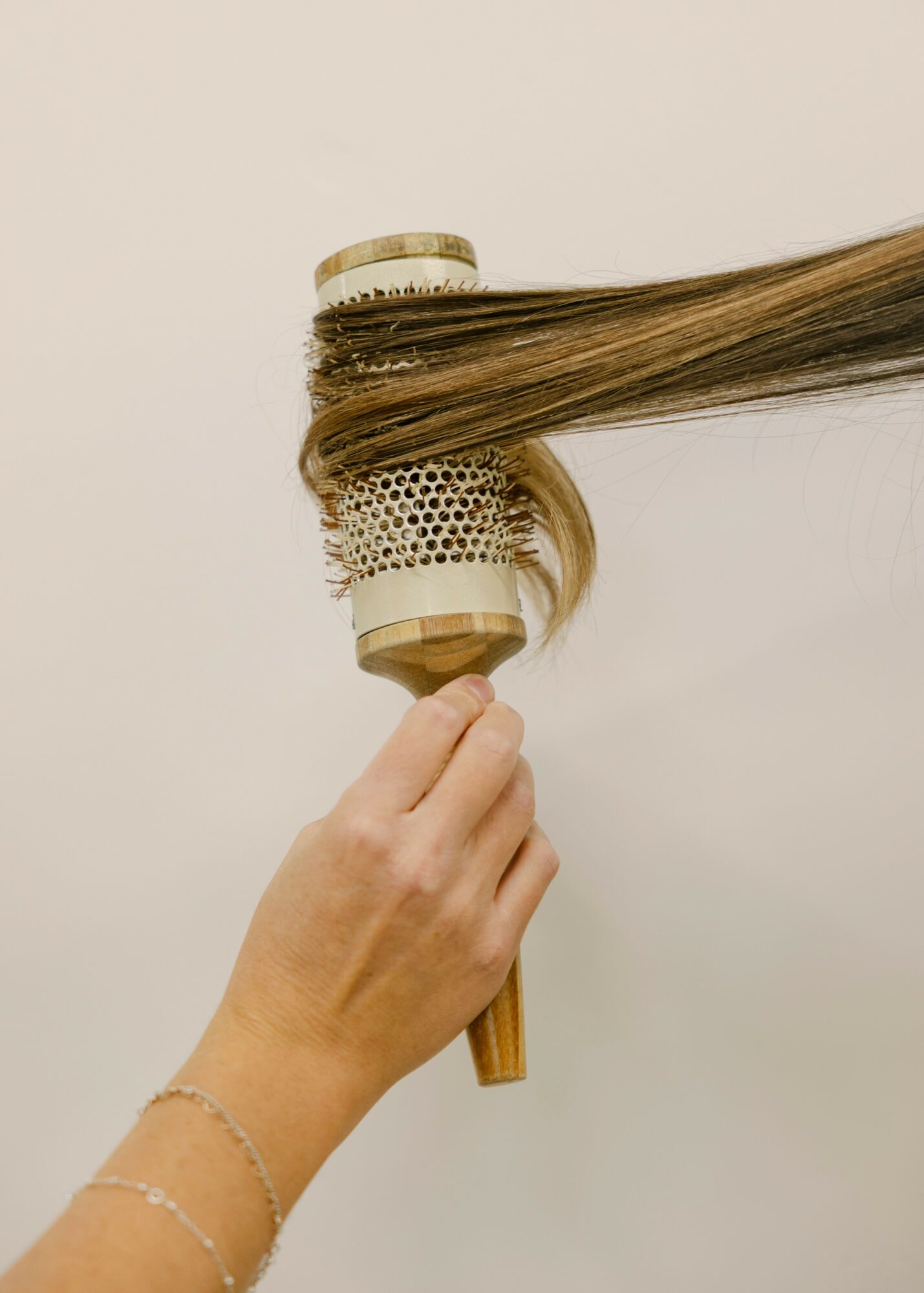 Person holding a round hairbrush with hair wrapped around it, against a plain white background.