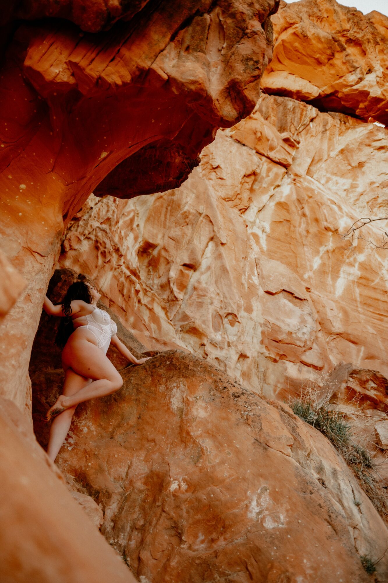 Person climbing large reddish and beige rocks outdoors, surrounded by natural rock formations.