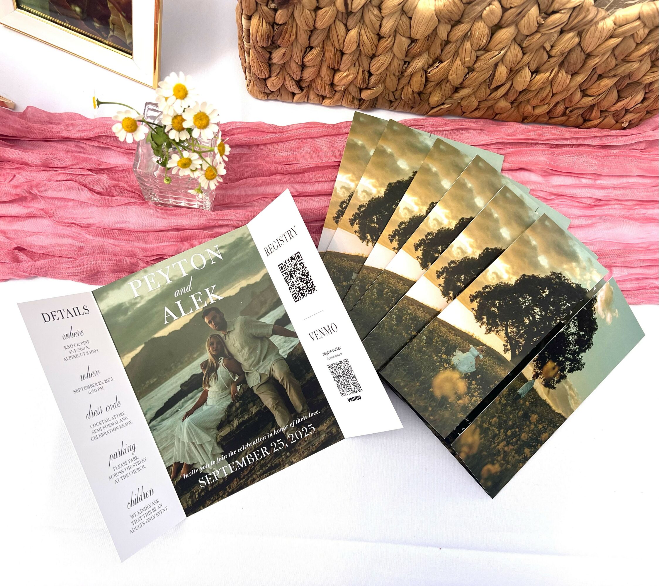Wedding invitation with a photo of a couple, floral details, and four landscape photographs, on a pink fabric background.