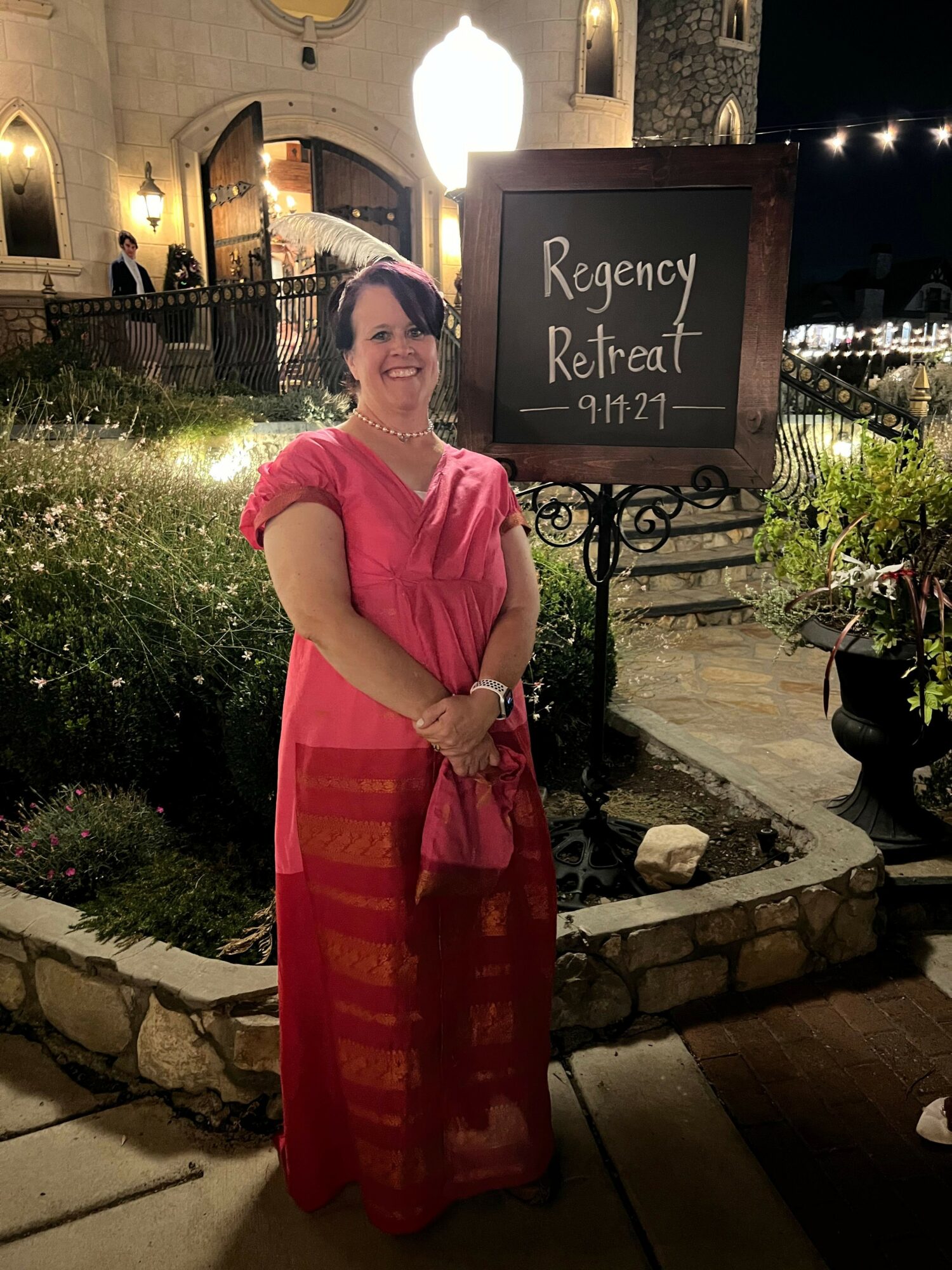Woman in pink dress standing outdoors near a sign for Regency Retreat Inn, illuminated at night.