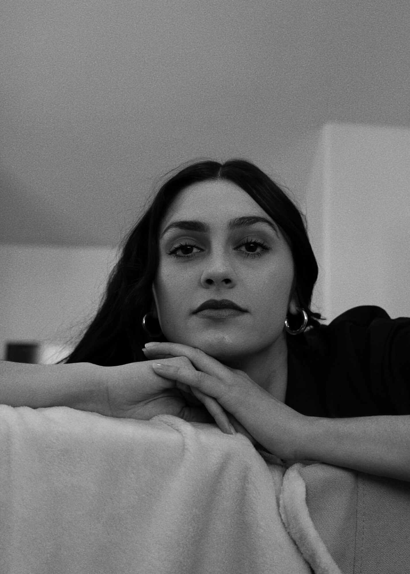 Woman with dark hair resting her head on a surface, looking at the camera, in black and white.