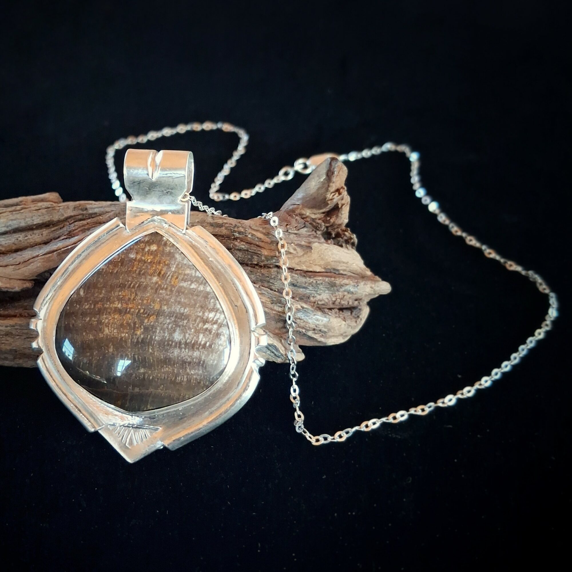 Silver pendant necklace with a large, round, clear gemstone, resting on a piece of wood against a black background.
